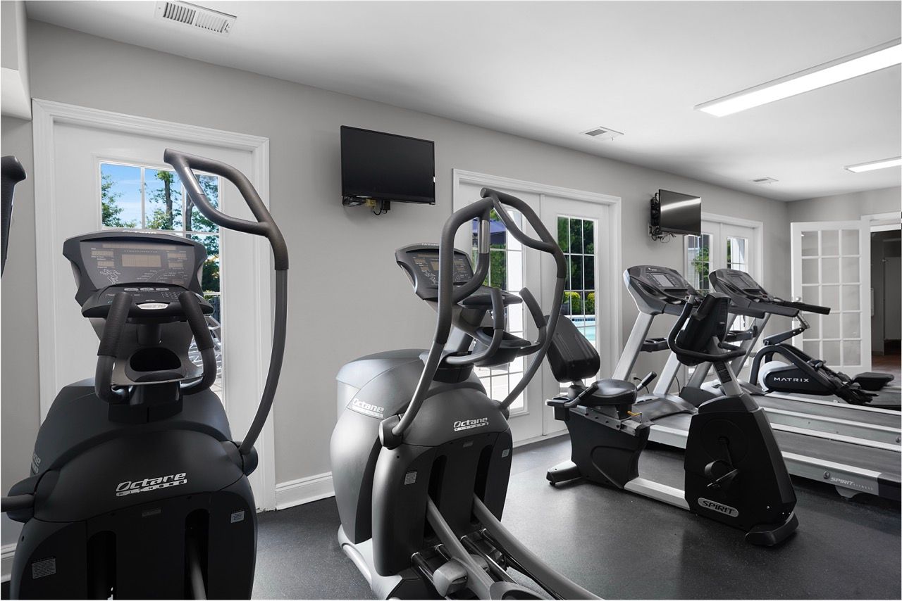 Interior view of a community fitness center with treadmills and ellipticals by windows.