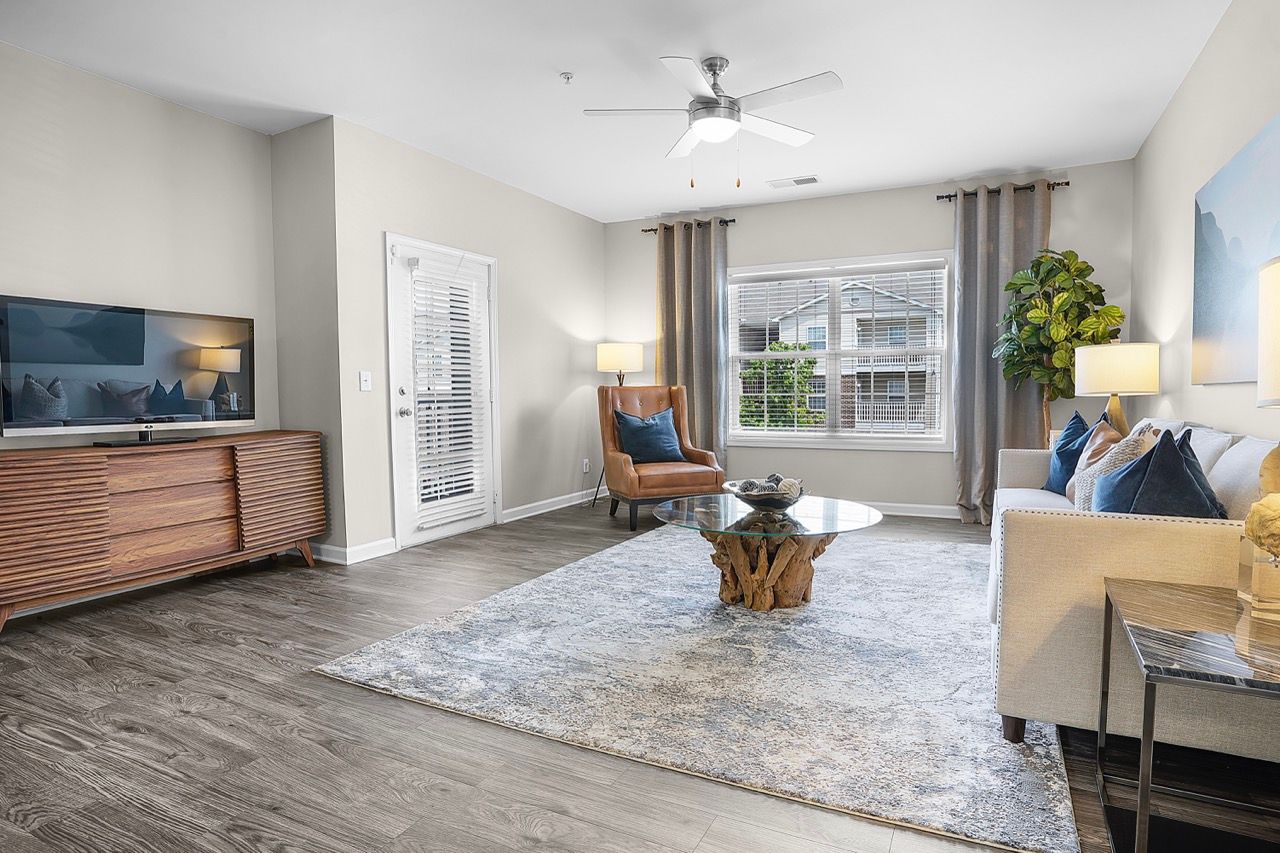 Living room with a sofa, armchair, glass coffee table, TV stand, and large window with curtains.