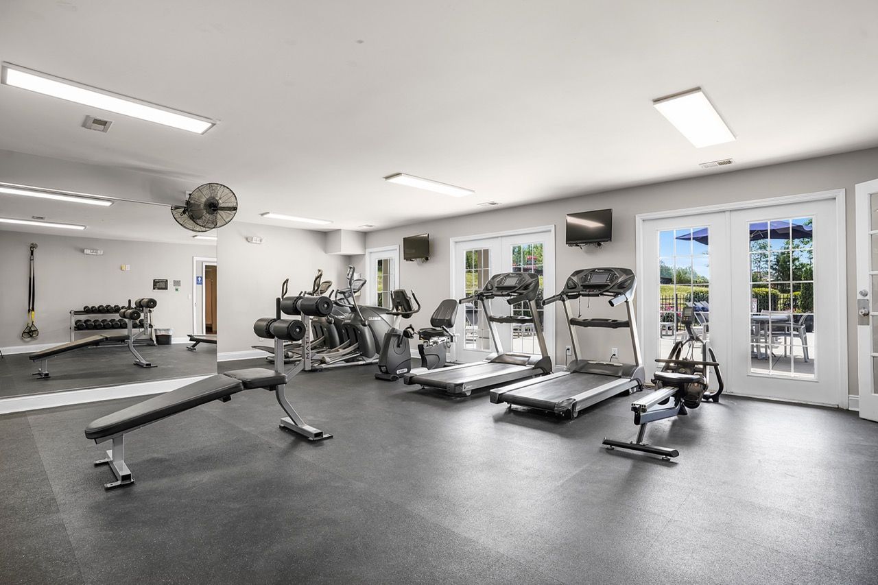 Interior community gym with cardio machines, free weights, and benches.