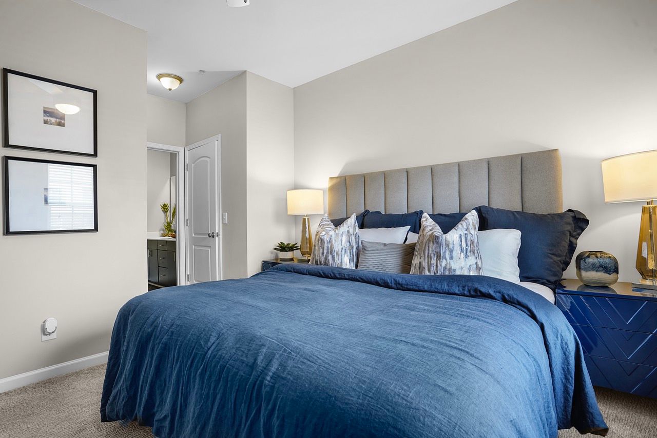 Bedroom with a large bed, blue duvet, upholstered headboard, and two matching nightstands with lamps.