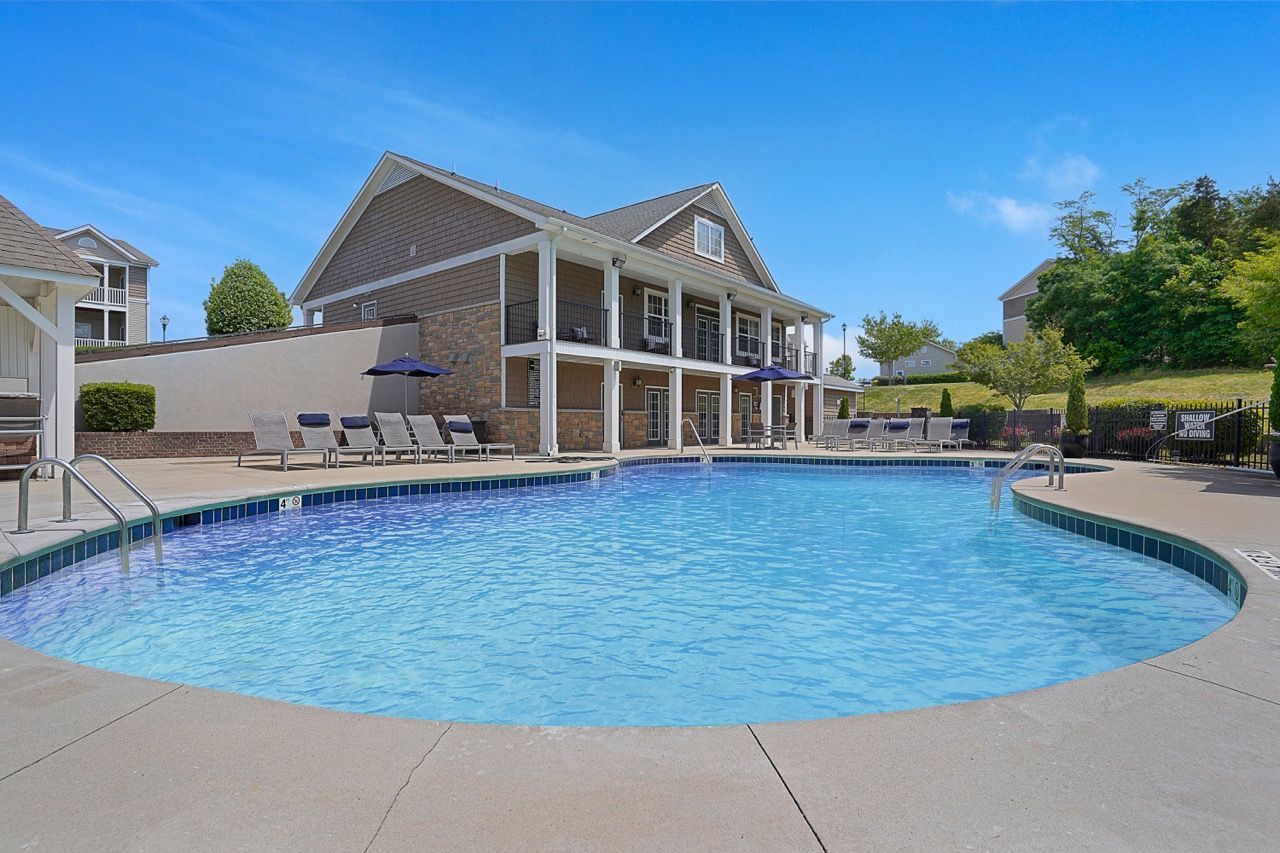 Outdoor apartment community pool with lounge chairs and a two-story clubhouse under a clear blue sky.