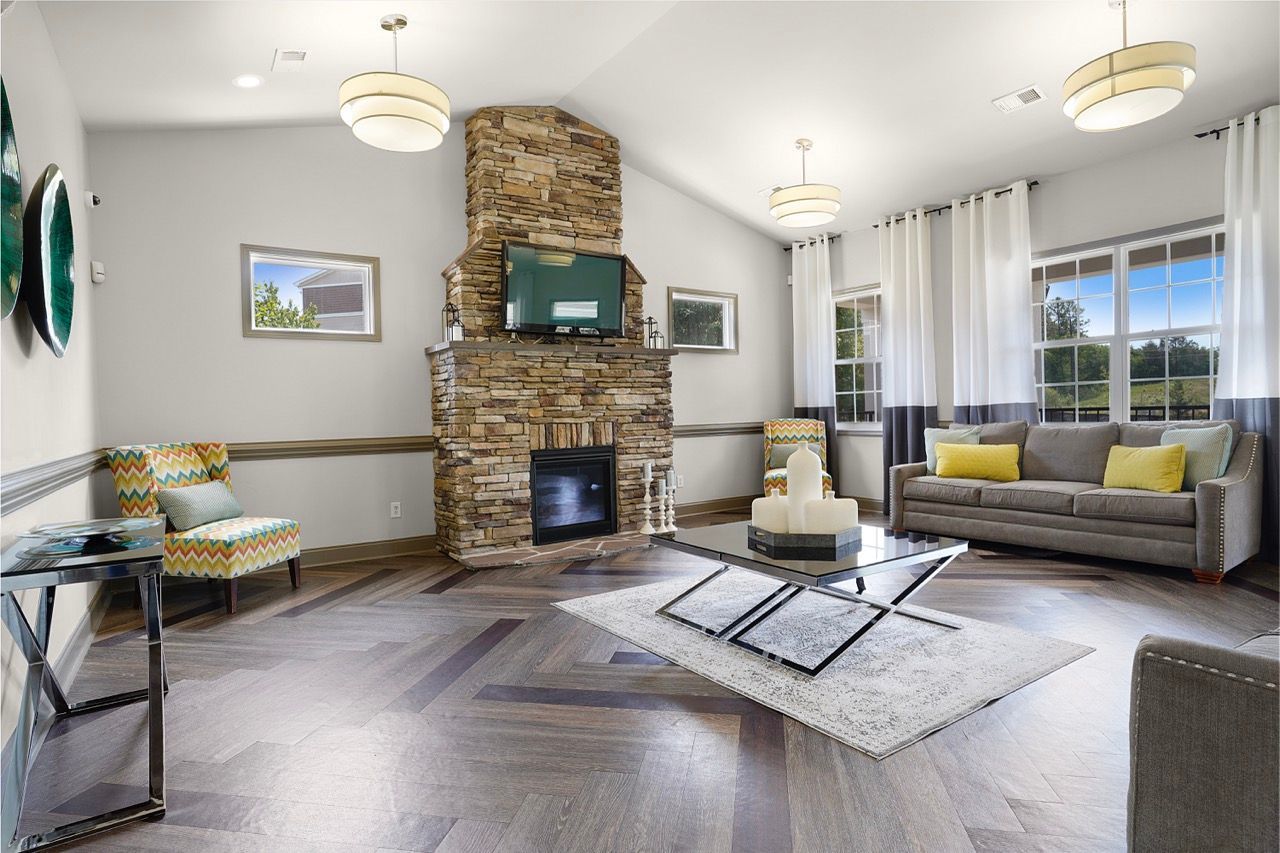 Living room with a stone fireplace, mounted TV, and large windows with white drapes.