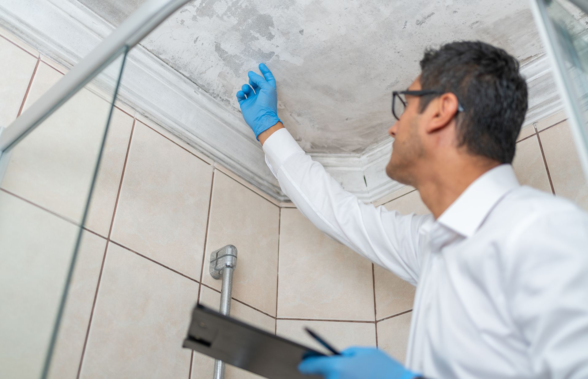 A man wearing blue gloves is looking at the ceiling of a bathroom - Bristol, VA - Keystone Home Inspections