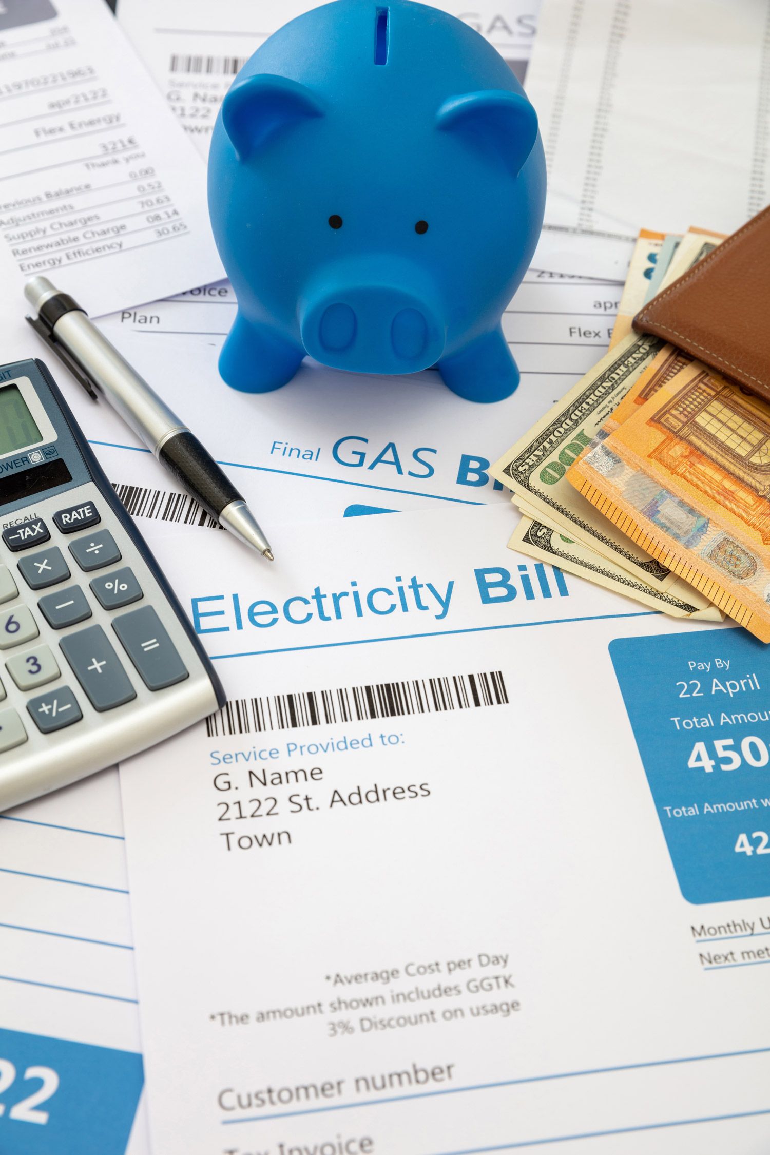 Blue piggy bank, bills, calculator, and cash sit on top of an electricity bill, representing financial planning and savings.