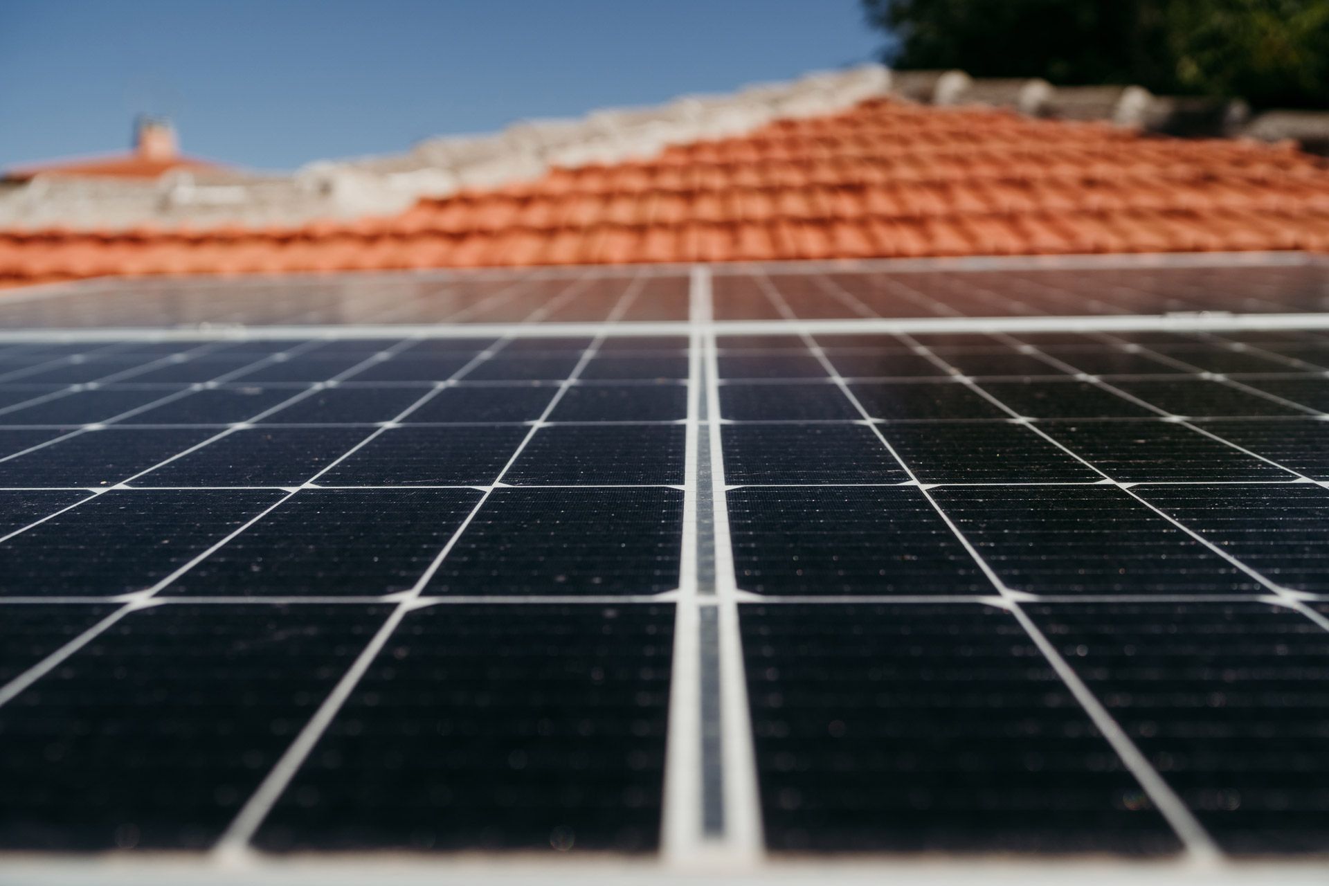 Solar panels installed on a rooftop with orange tiles, under a clear blue sky.