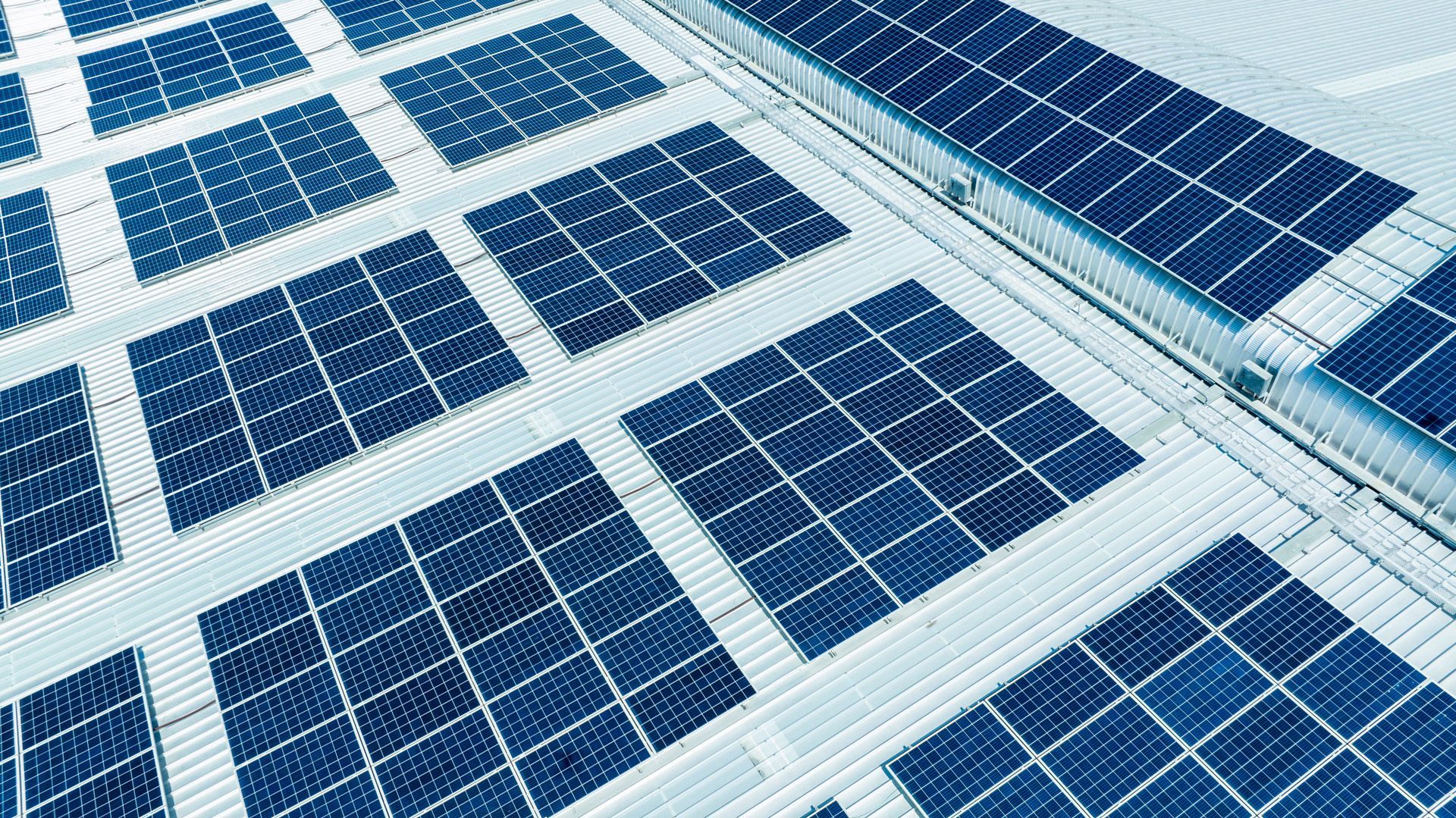 Solar panels arranged in neat rows on a building roof. The panels are dark blue.
