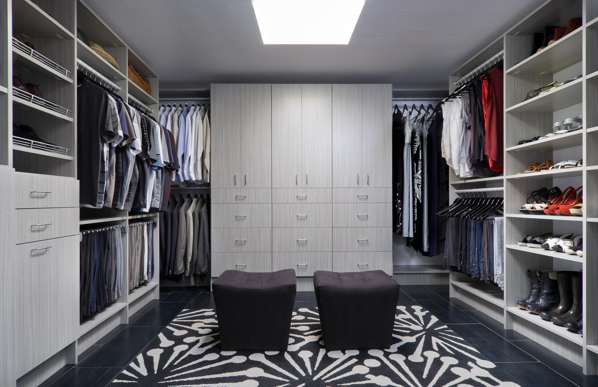 a walk in closet with lots of clothes and two ottomans