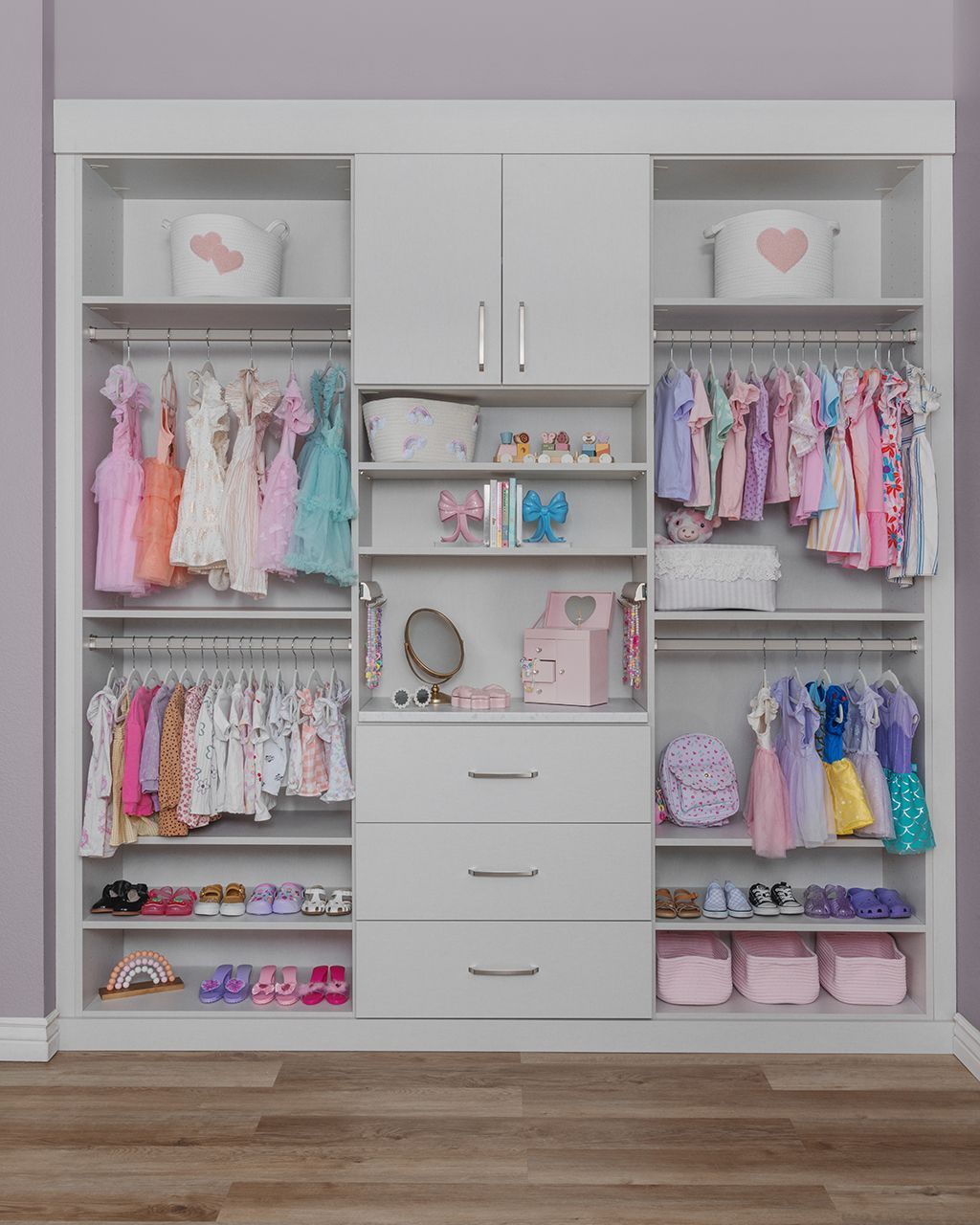 White built-in closet with pastel children's clothes, shoes, and storage bins neatly arranged on shelves and rods