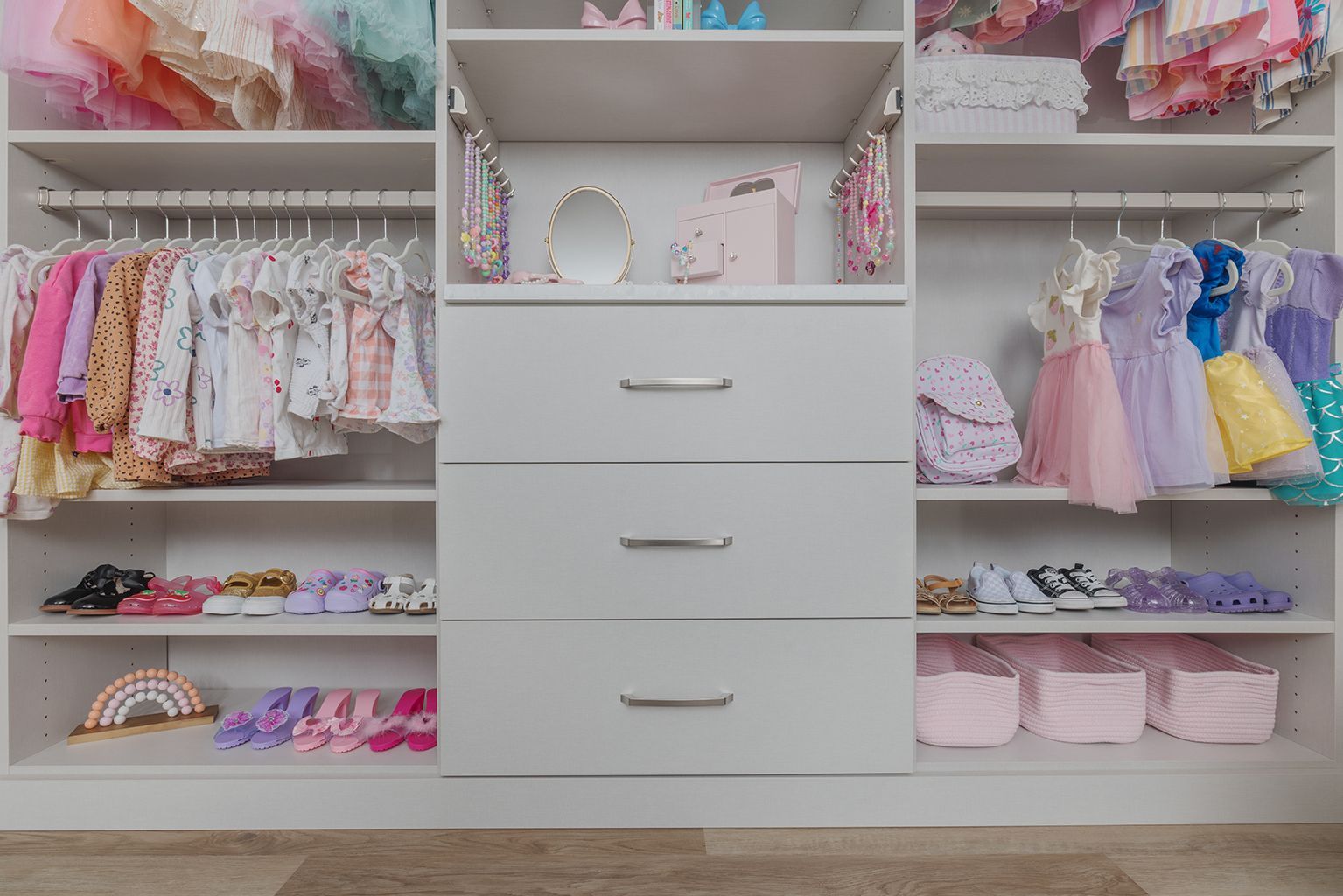 Pink and pastel children’s closet with dresses, folded clothes, shoes, and drawers