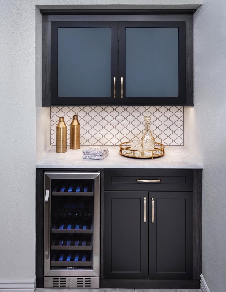 Built-in bar with a wine fridge, cabinets, and decorative items. Black cabinets with glass doors, white tile backsplash.