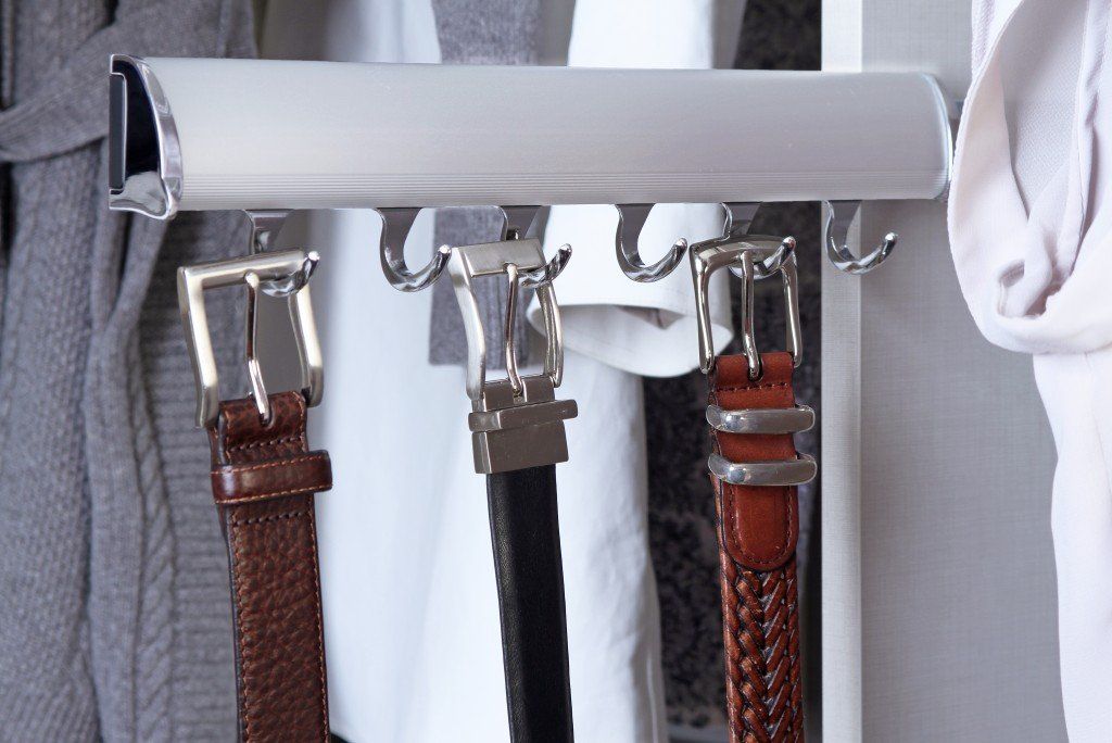 three brown belts are hanging on hooks in a closet