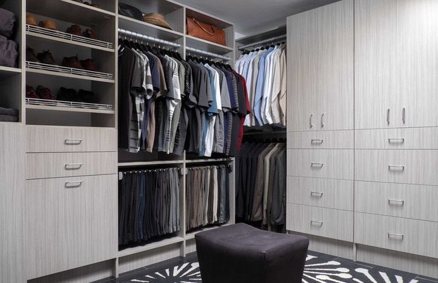 A walk in closet filled with lots of clothes and a black ottoman.