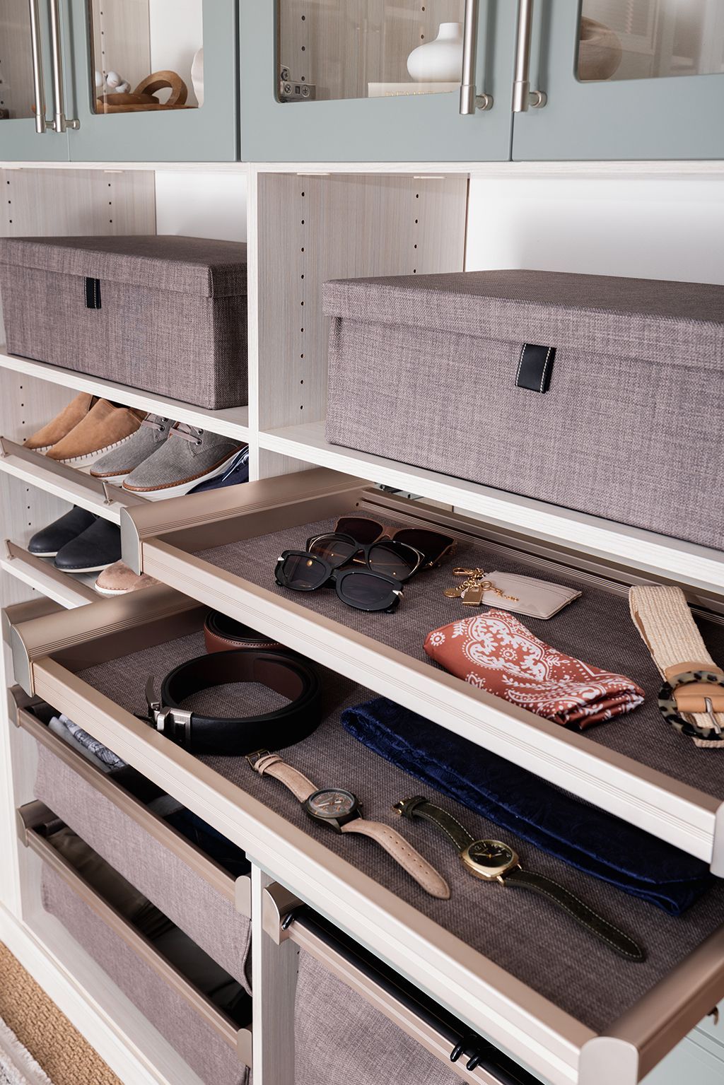Open closet drawers with belts, accessories, and folded clothes in gray organizers.