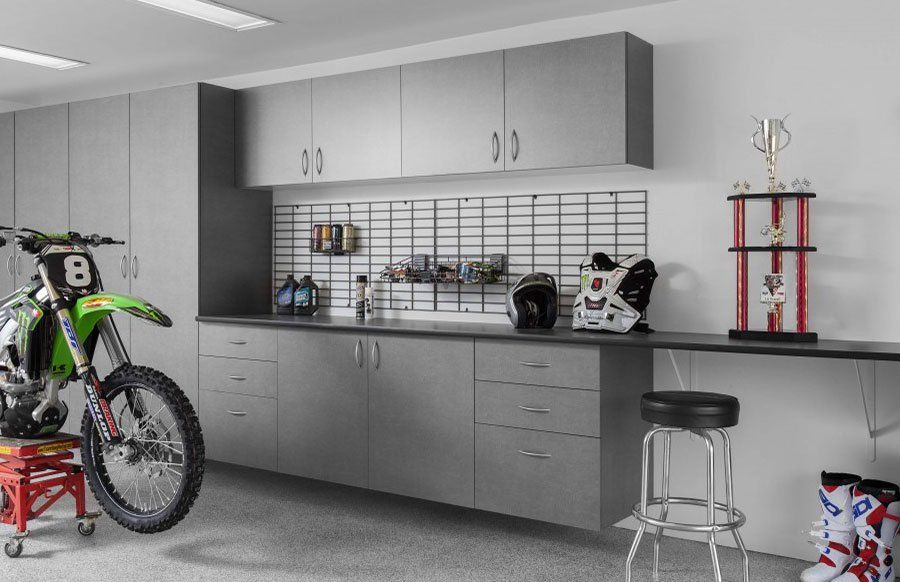 a dirt bike is parked in a garage next to garage cabinets and a workbench.