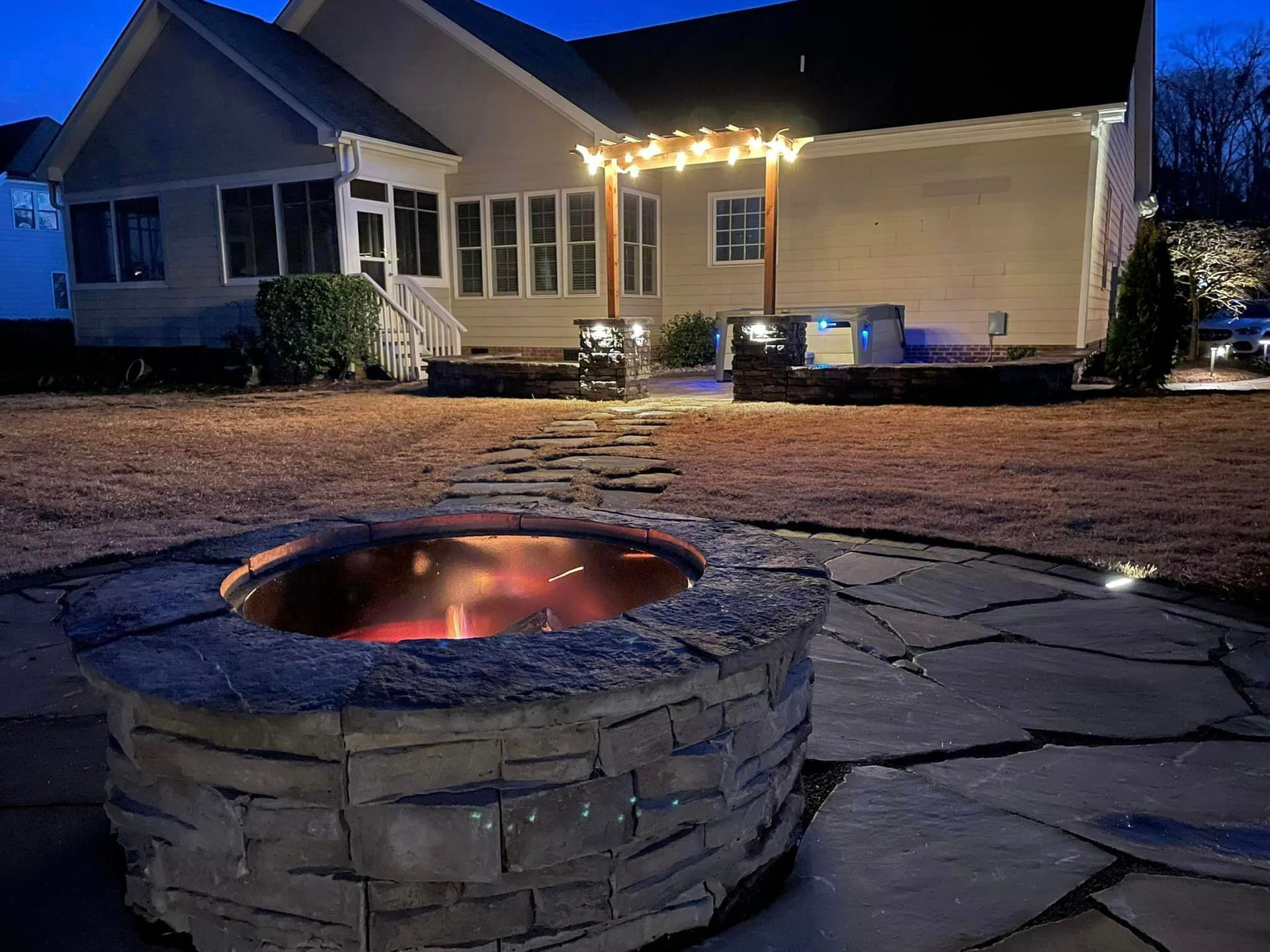 A fire pit is lit up in front of a house at night.