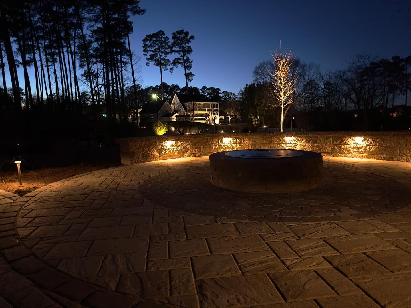 A fire pit is lit up at night with a house in the background.