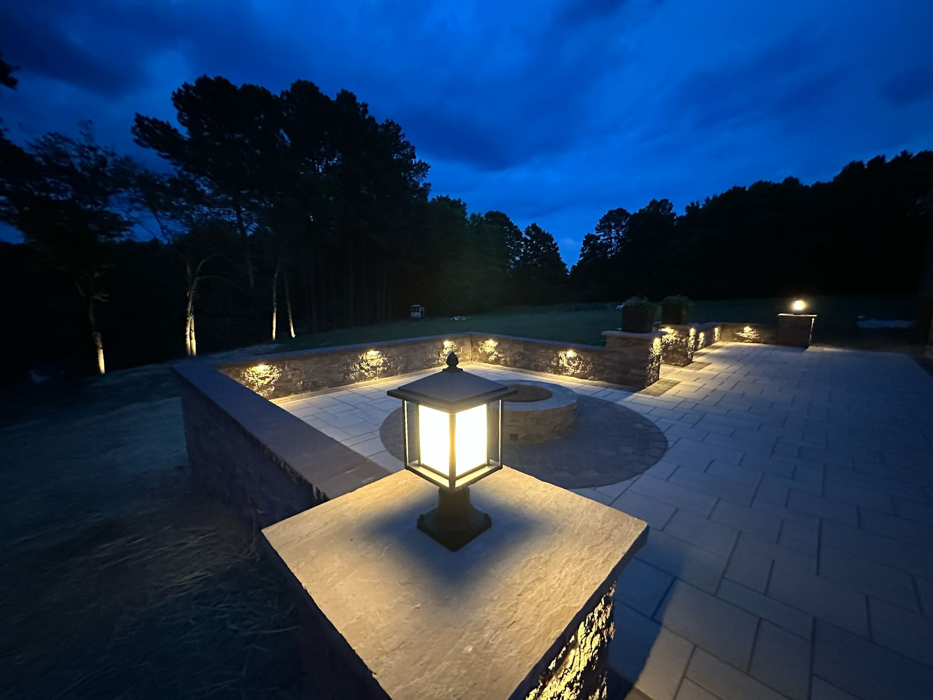 A patio is lit up at night with trees in the background