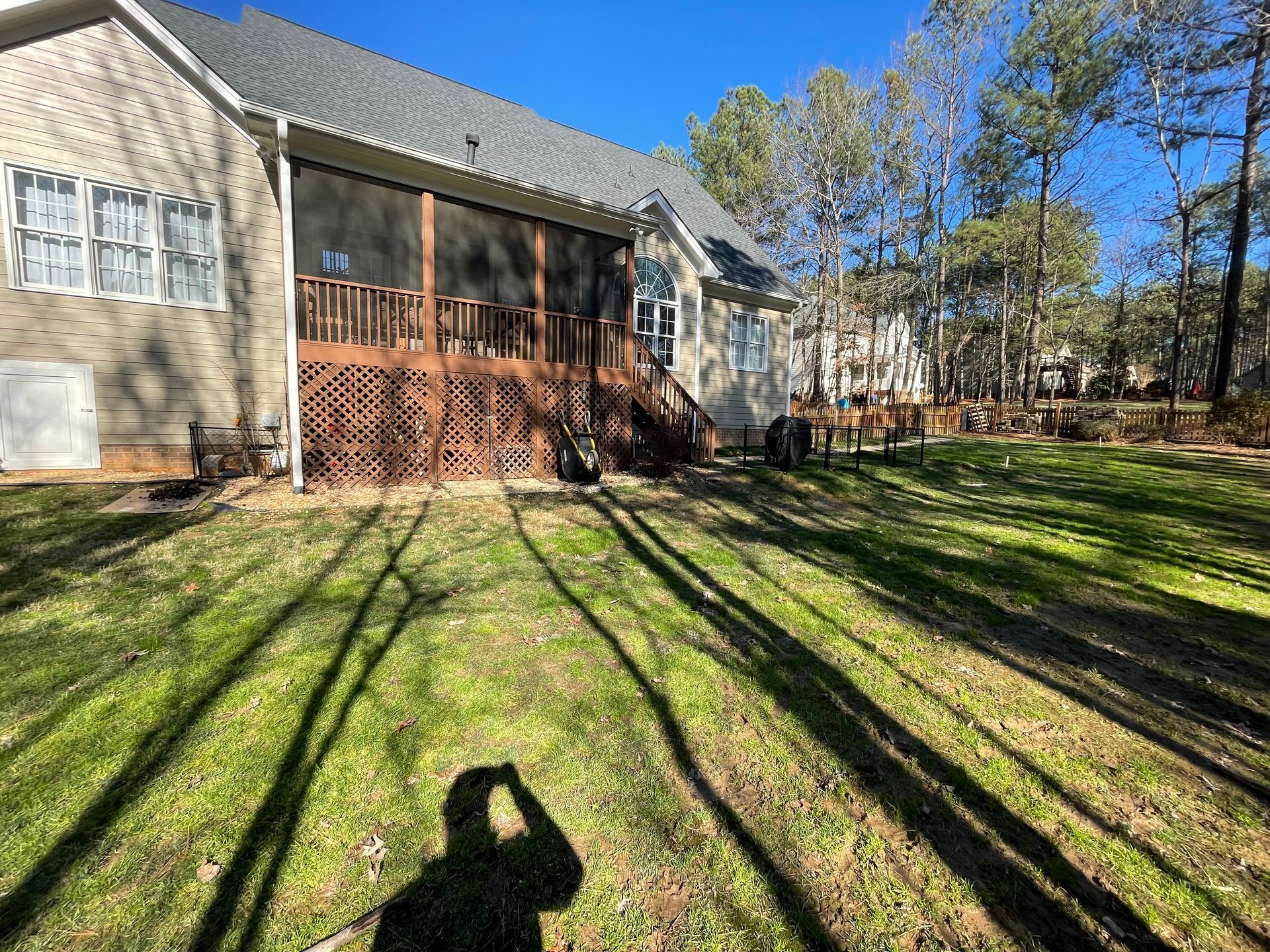 A shadow of a person is cast on the grass in front of a house.