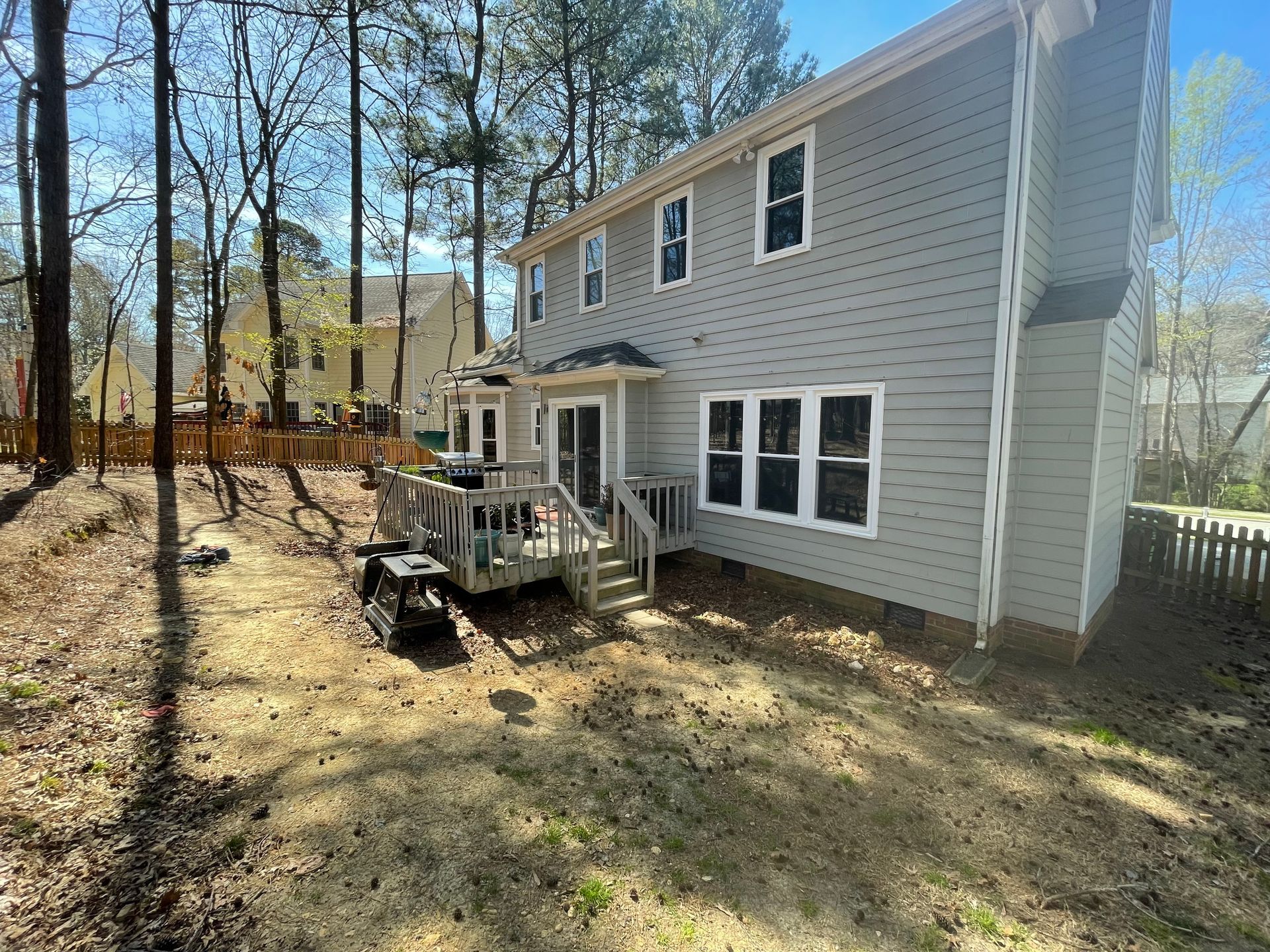 The back of a house with a deck in the backyard surrounded by trees.
