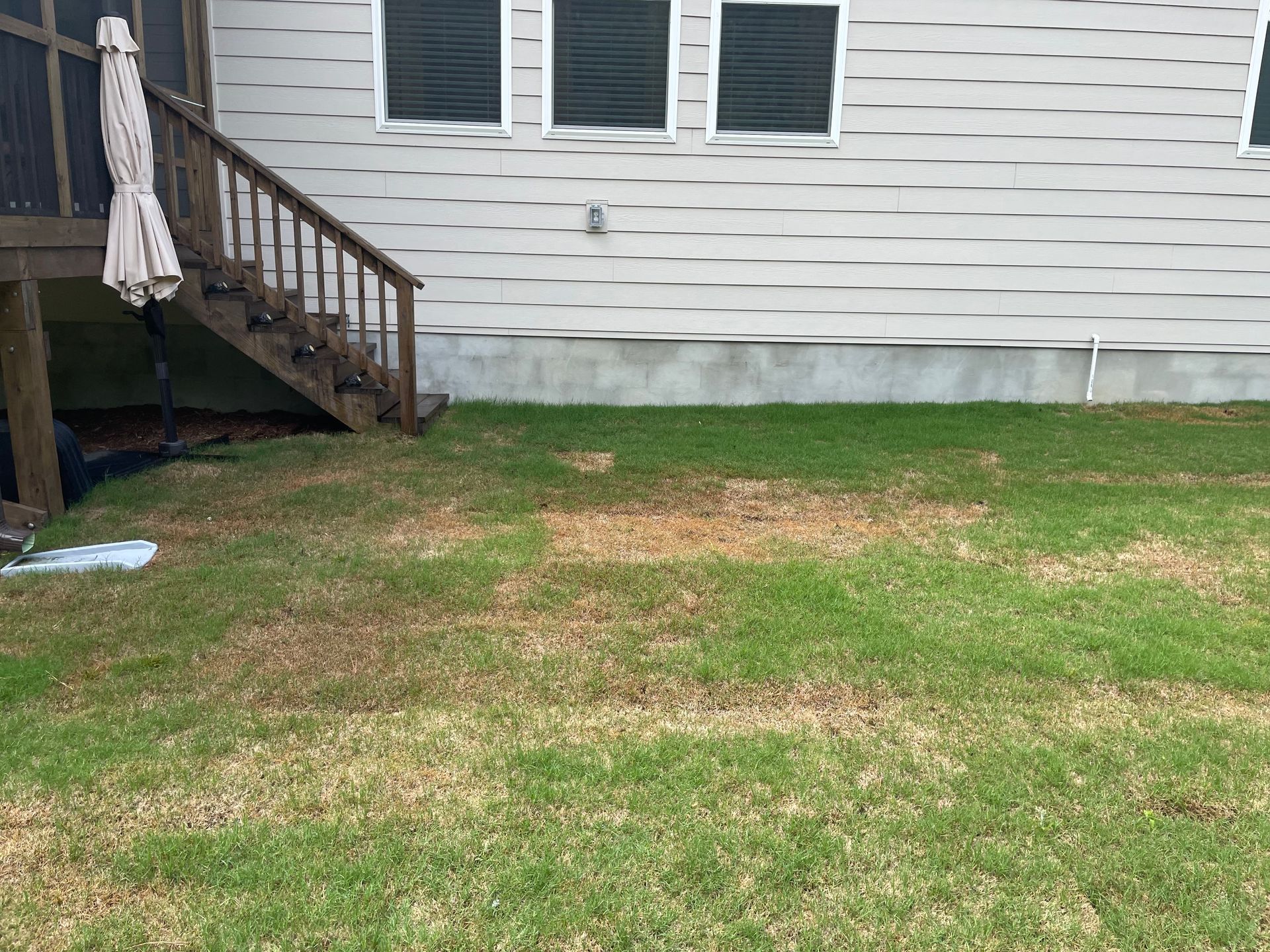 A lawn with a deck and stairs in front of a house.