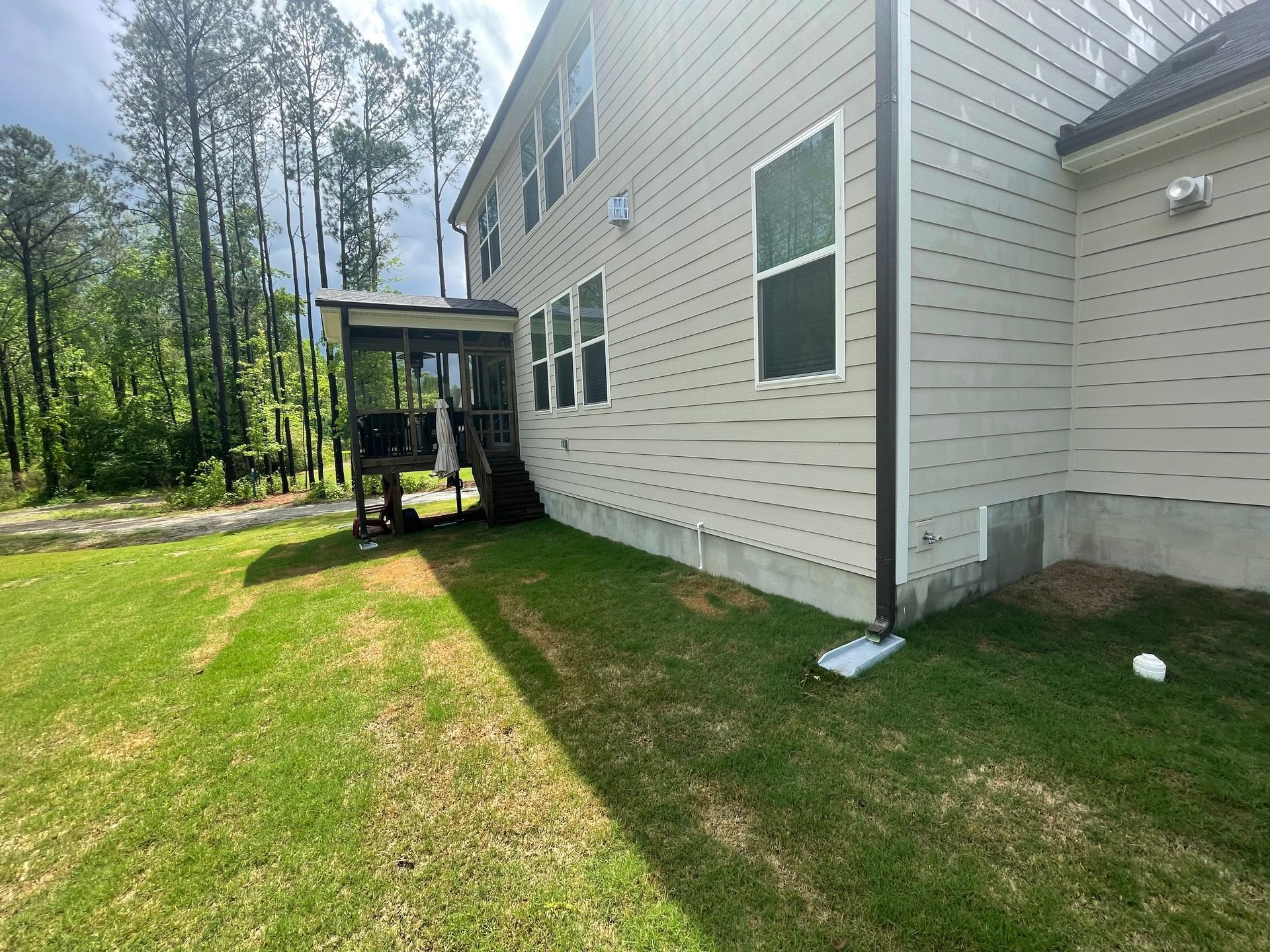The backyard of a house with a large lawn and trees in the background.
