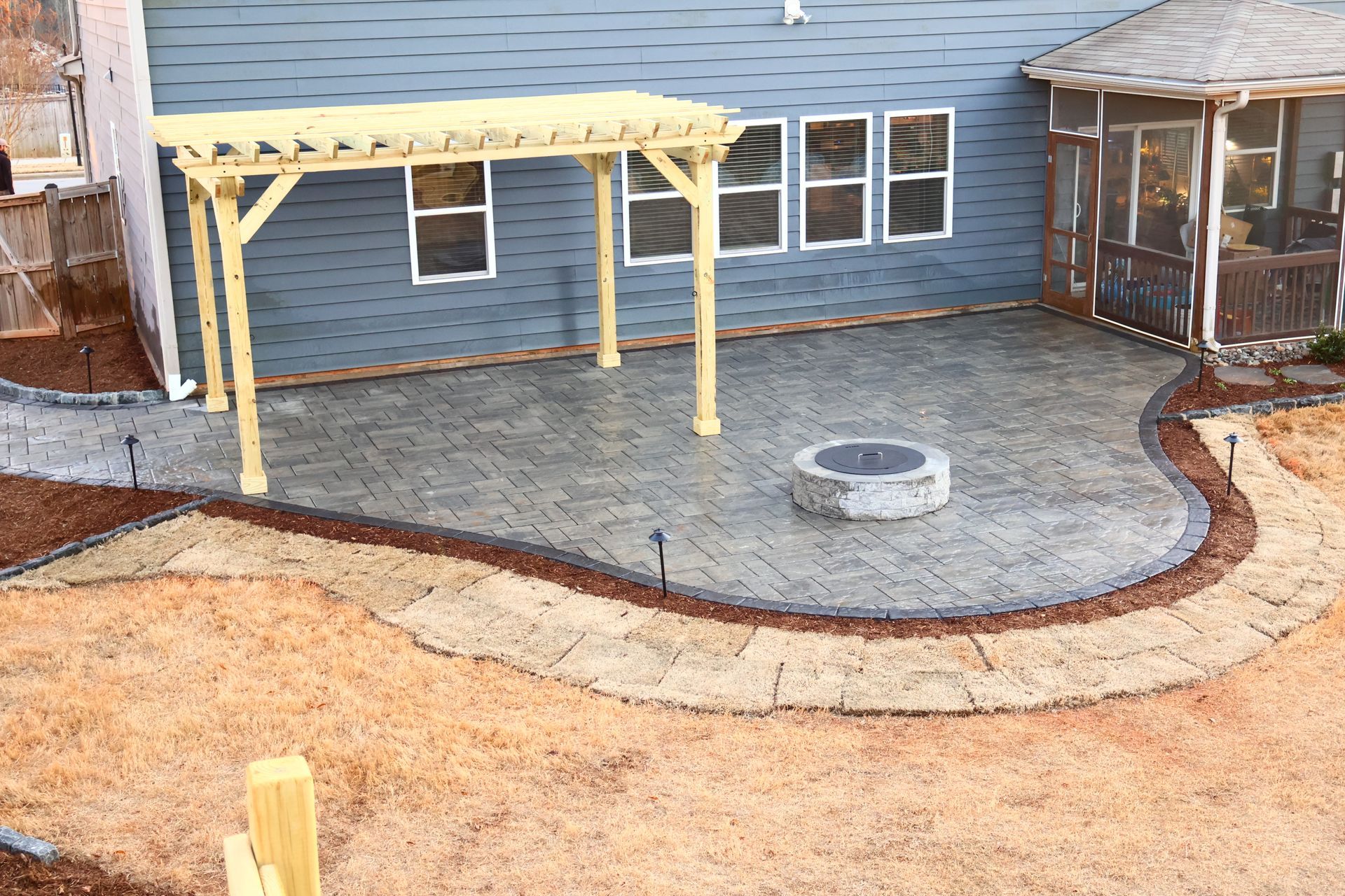 A patio with a fire pit and a pergola in front of a house.