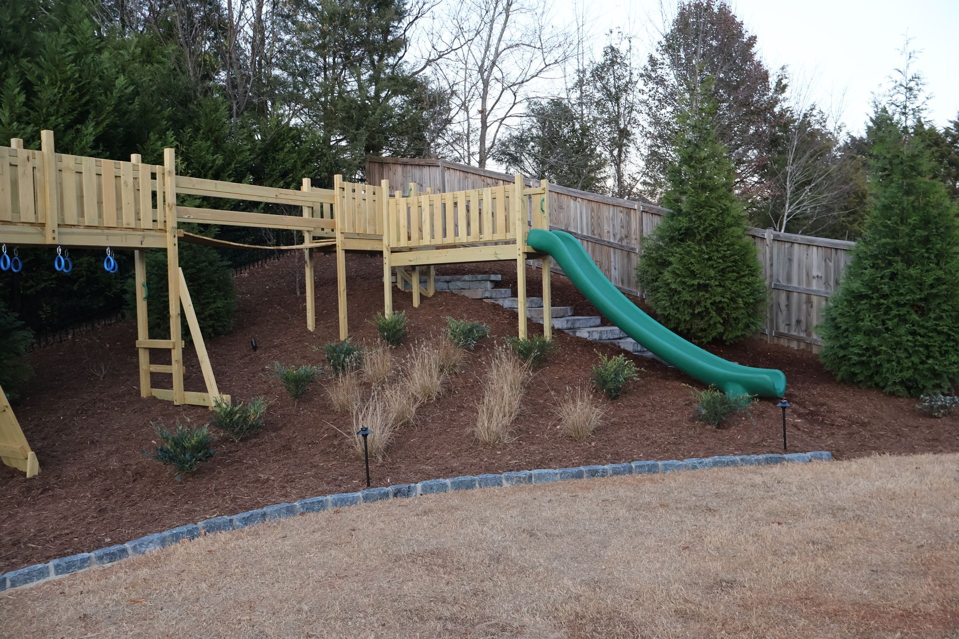 A wooden playground with a green slide and stairs