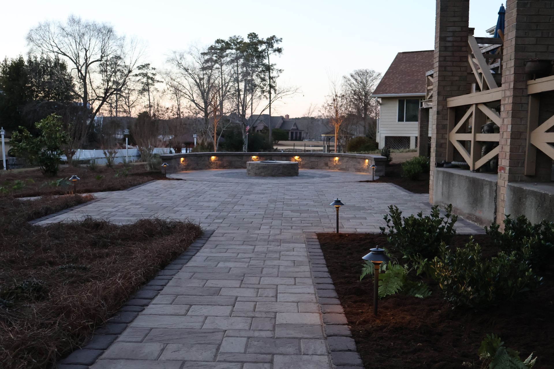 A brick walkway leading to a house with trees in the background