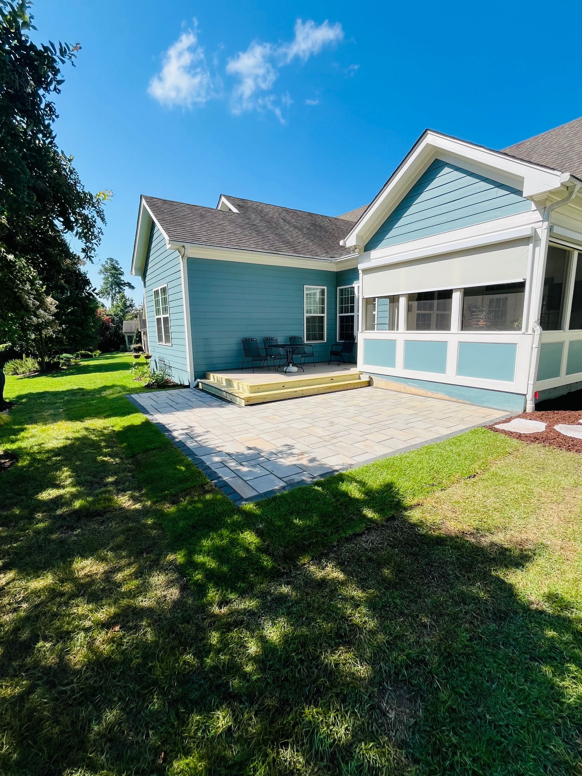 Blue house with patio and screened porch, on grassy lawn under a sunny sky.