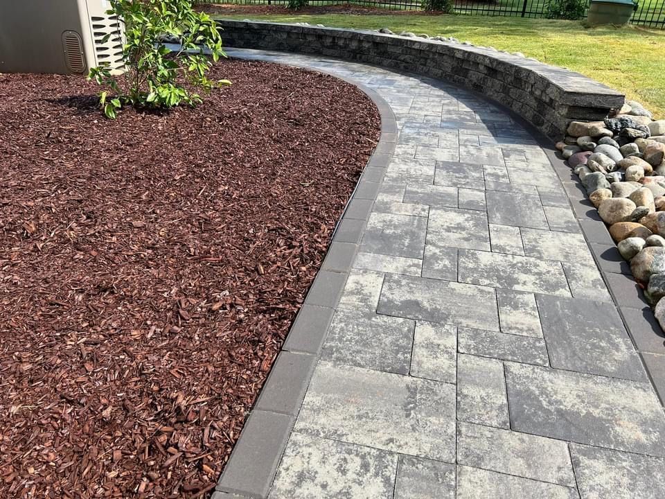 A brick walkway leading to a stone wall surrounded by rocks and mulch.