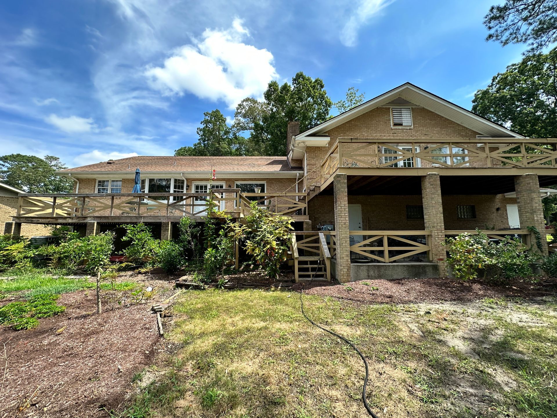 A large house with a large porch is surrounded by trees on a sunny day.