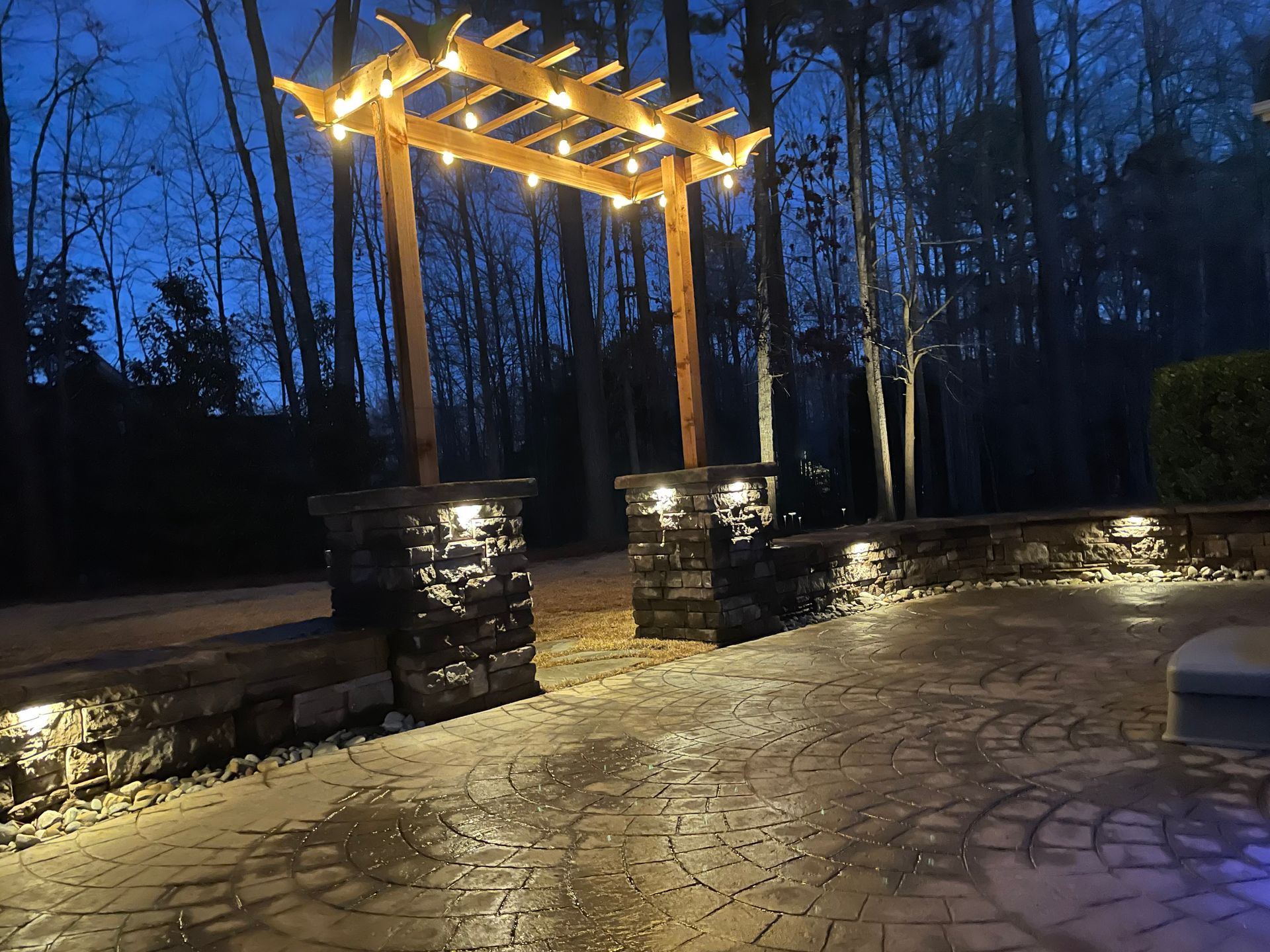 A pergola is lit up at night in a backyard.