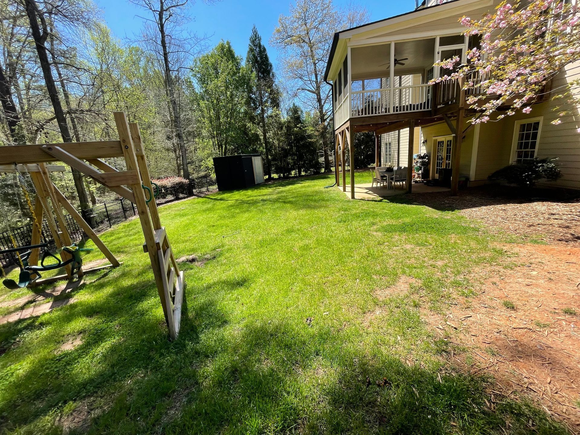 A large yard with a house in the background and a swing set in the foreground.