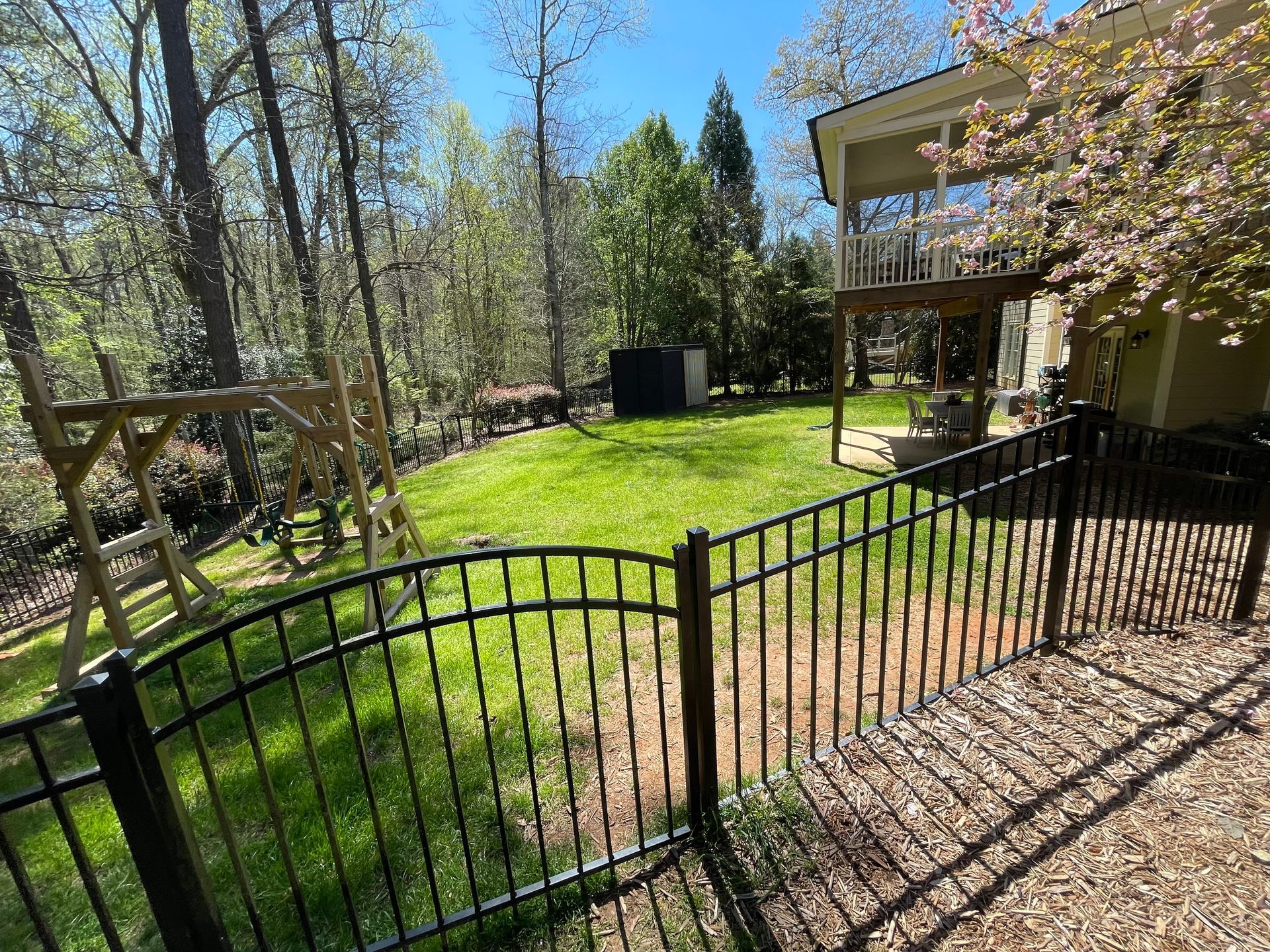 A black fence surrounds a lush green yard in front of a house.