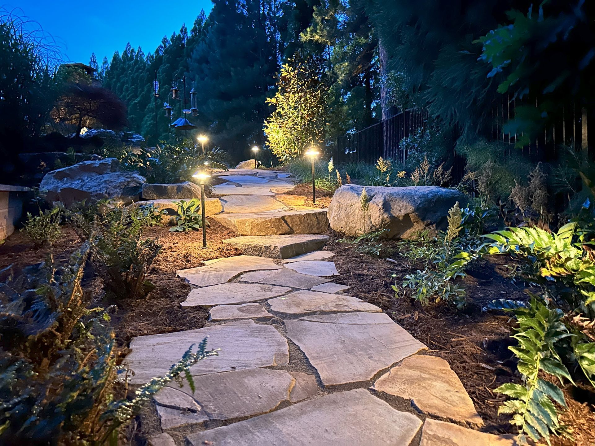 A stone walkway is lit up at night in a garden.