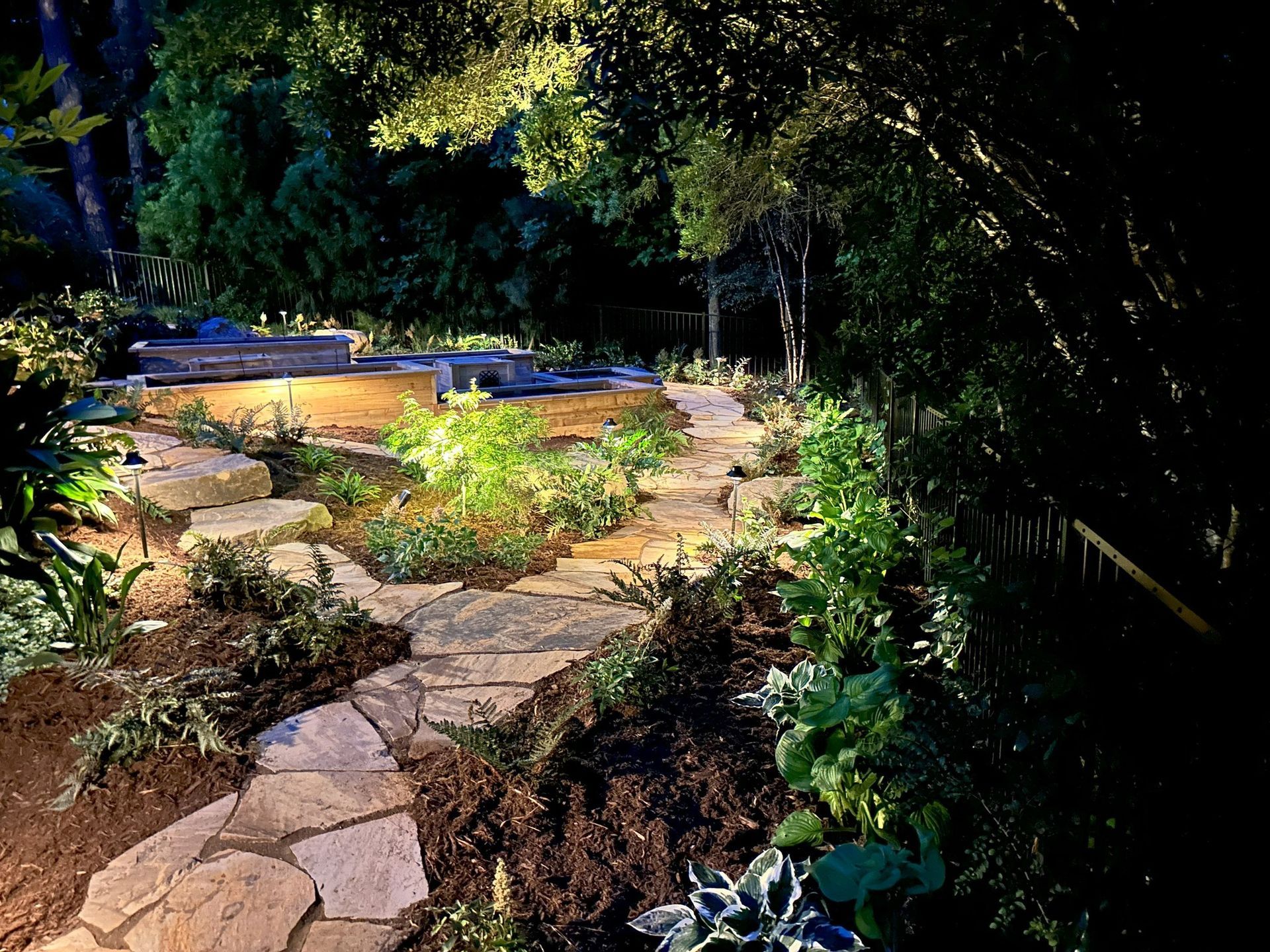 A stone walkway is lit up at night in a garden surrounded by trees.