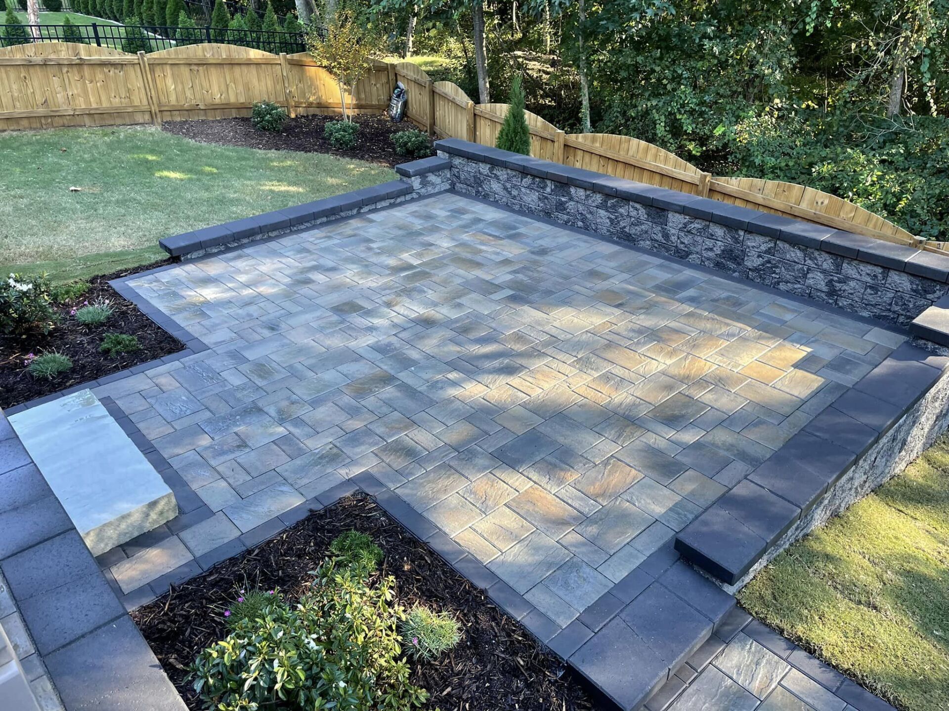 A patio with a stone wall and a bench in a backyard.