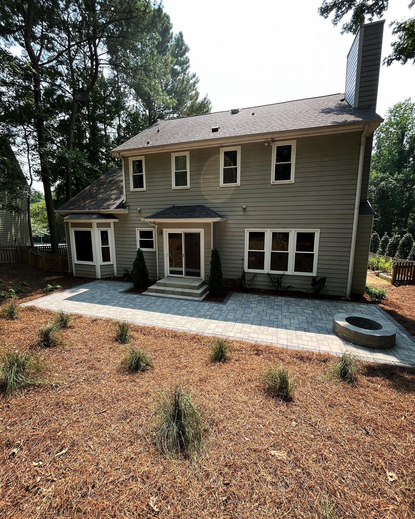 A large house with a fire pit in the backyard surrounded by trees.