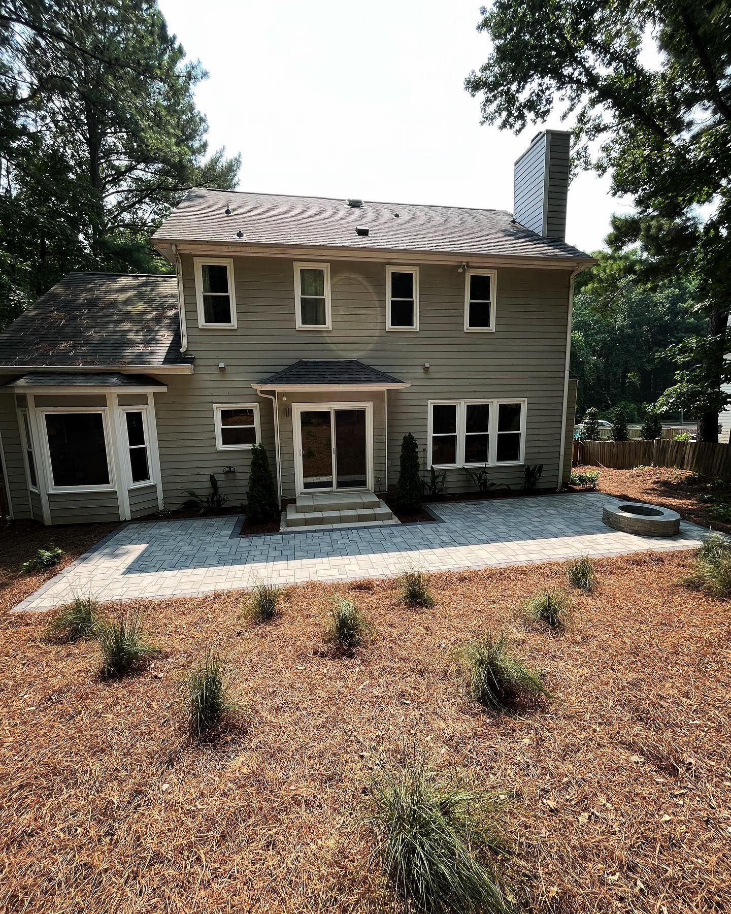 The back of a house with a patio and trees in the background.
