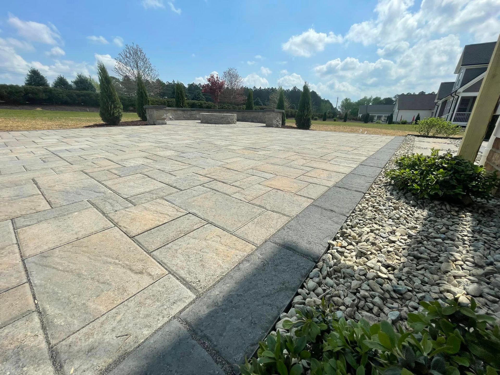 A patio with a gravel border and trees in the background on a sunny day.