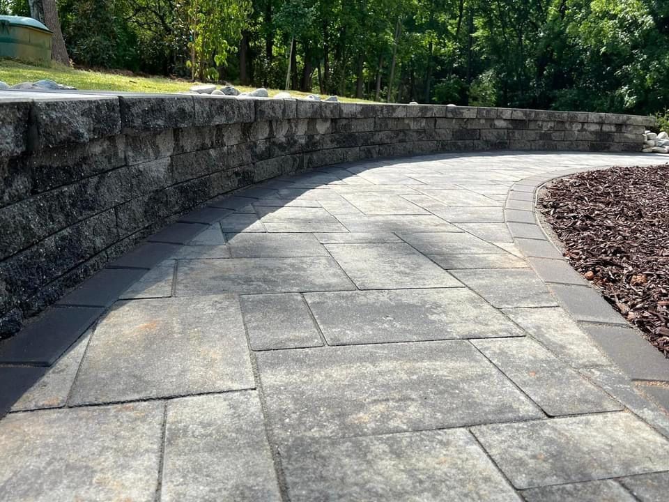 A stone walkway leading to a stone wall with trees in the background.