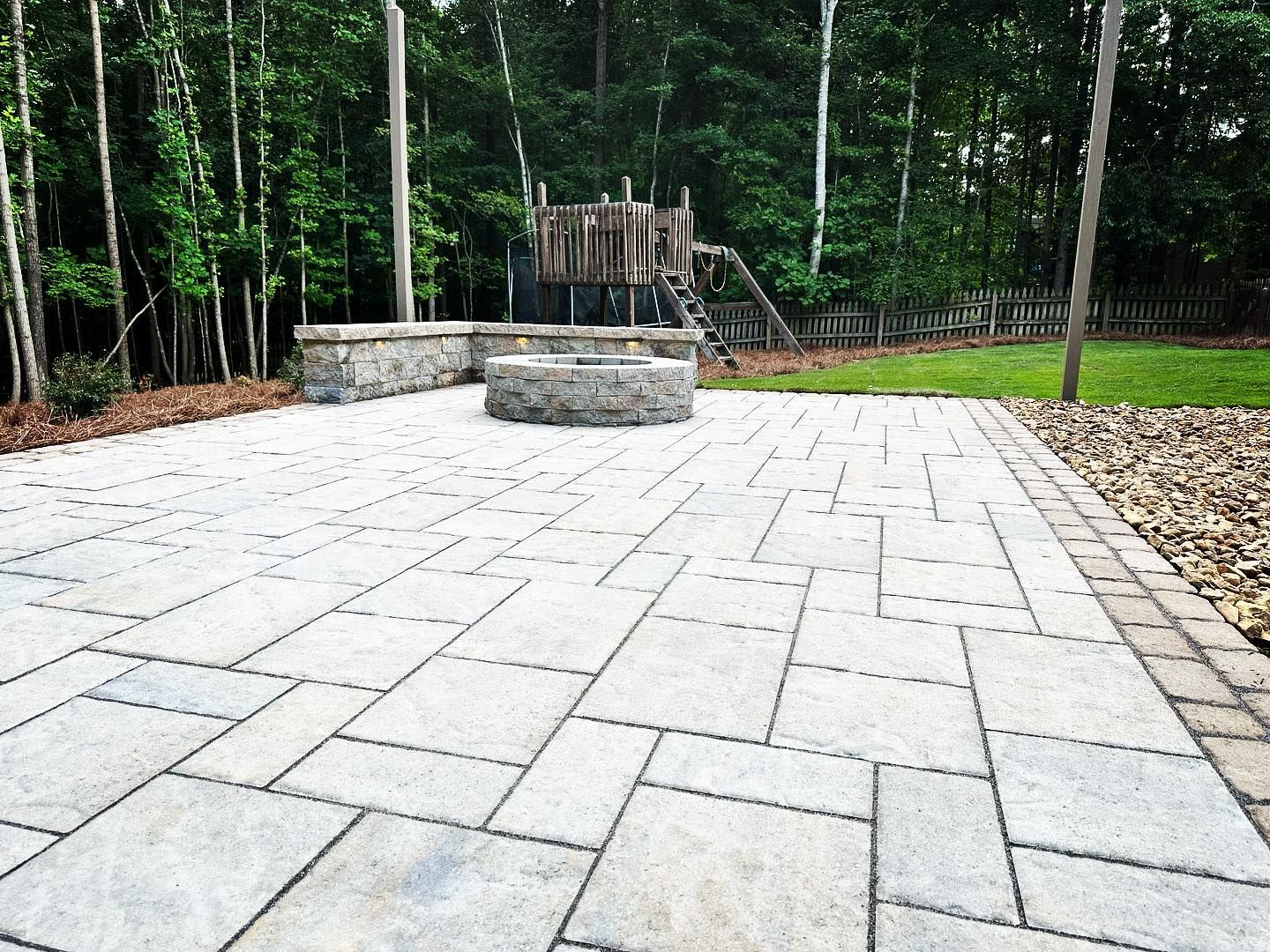 A patio with a fire pit and a playground in the background