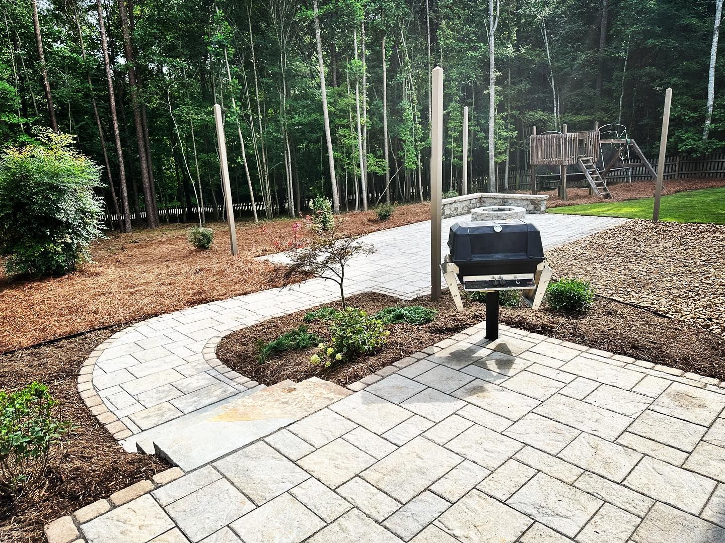 A grill is sitting on a patio next to a path in the woods.