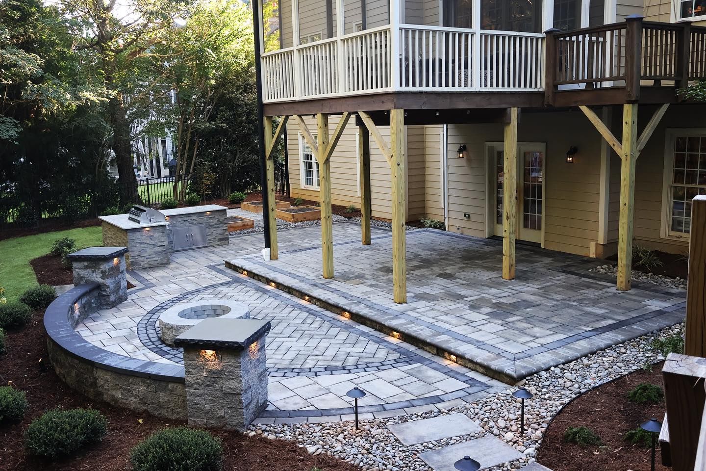 A patio with a fire pit and a deck in the backyard of a house.