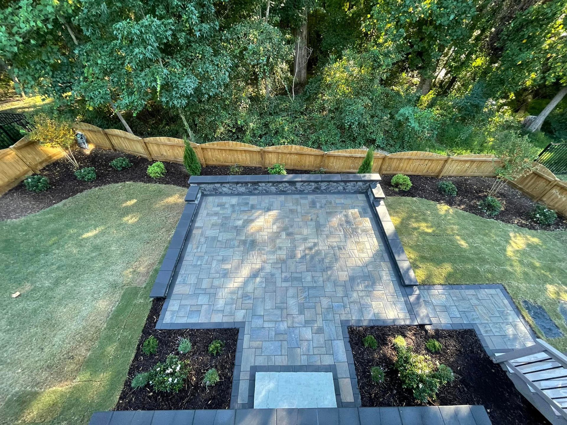 An aerial view of a backyard with a brick patio and a wooden fence.