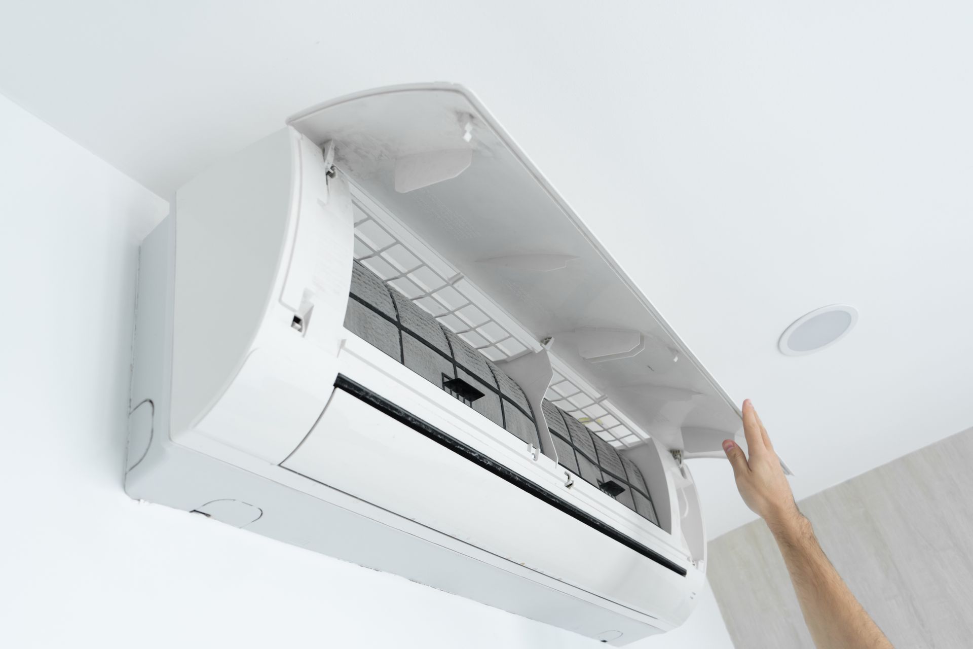 A hand opening the cover of a white wall-mounted air conditioning unit.