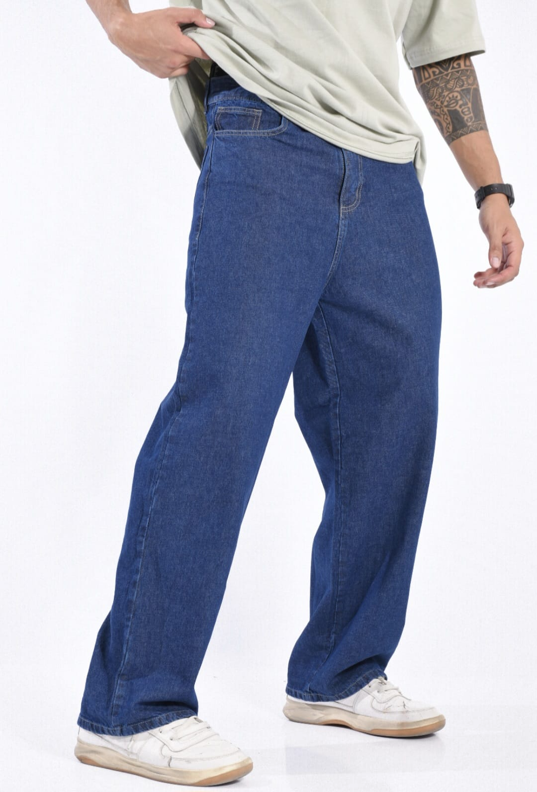 Persona vestida con vaqueros azules y zapatillas blancas, de pie en una pose informal.