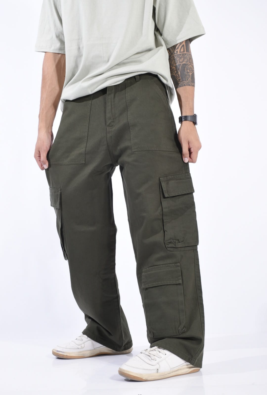 Persona con camisa clara y pantalones cargo color oliva con zapatillas blancas, de pie sobre un fondo blanco.