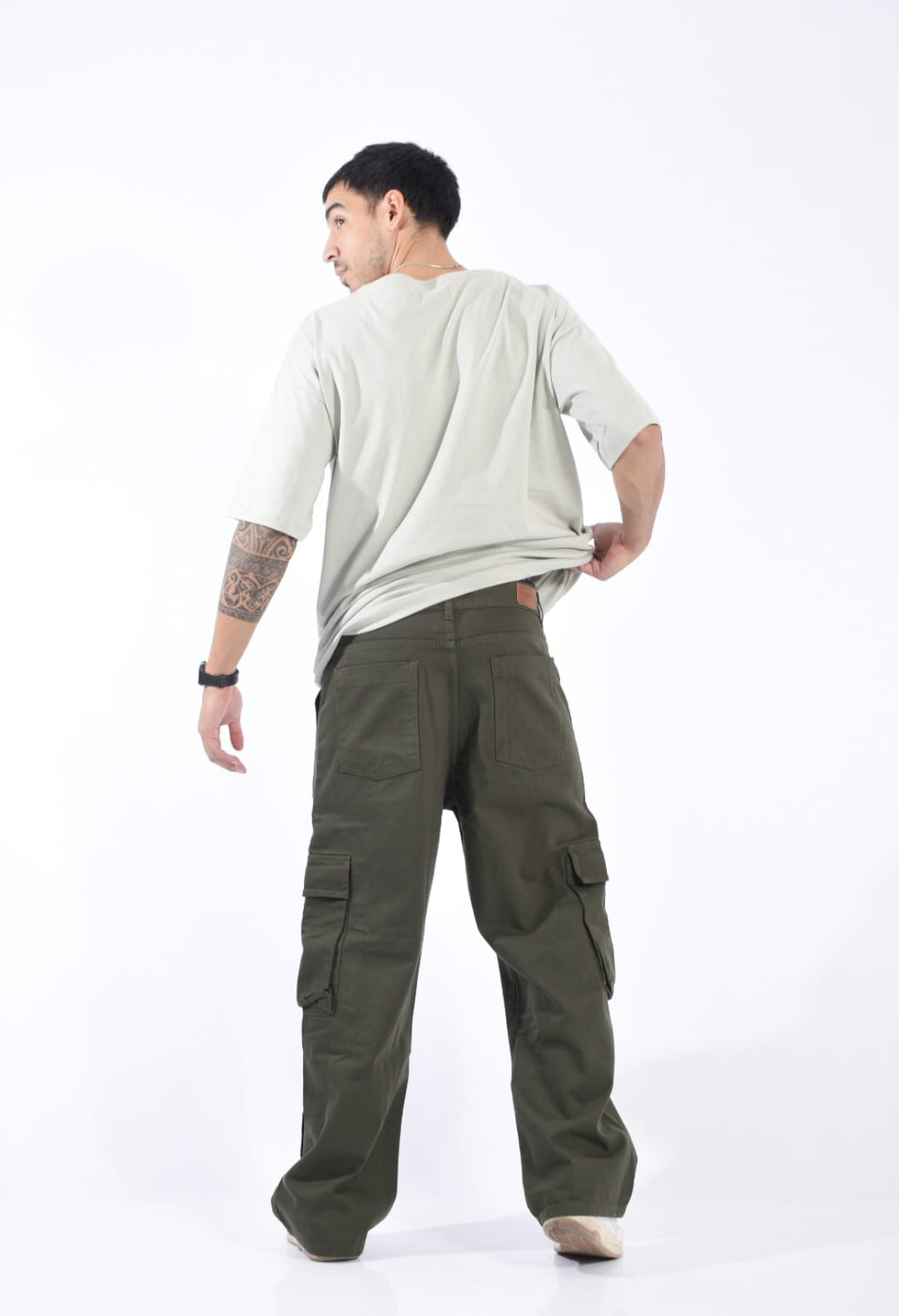 Persona con camisa clara y pantalones cargo color oliva con zapatillas blancas, de pie sobre un fondo blanco.
