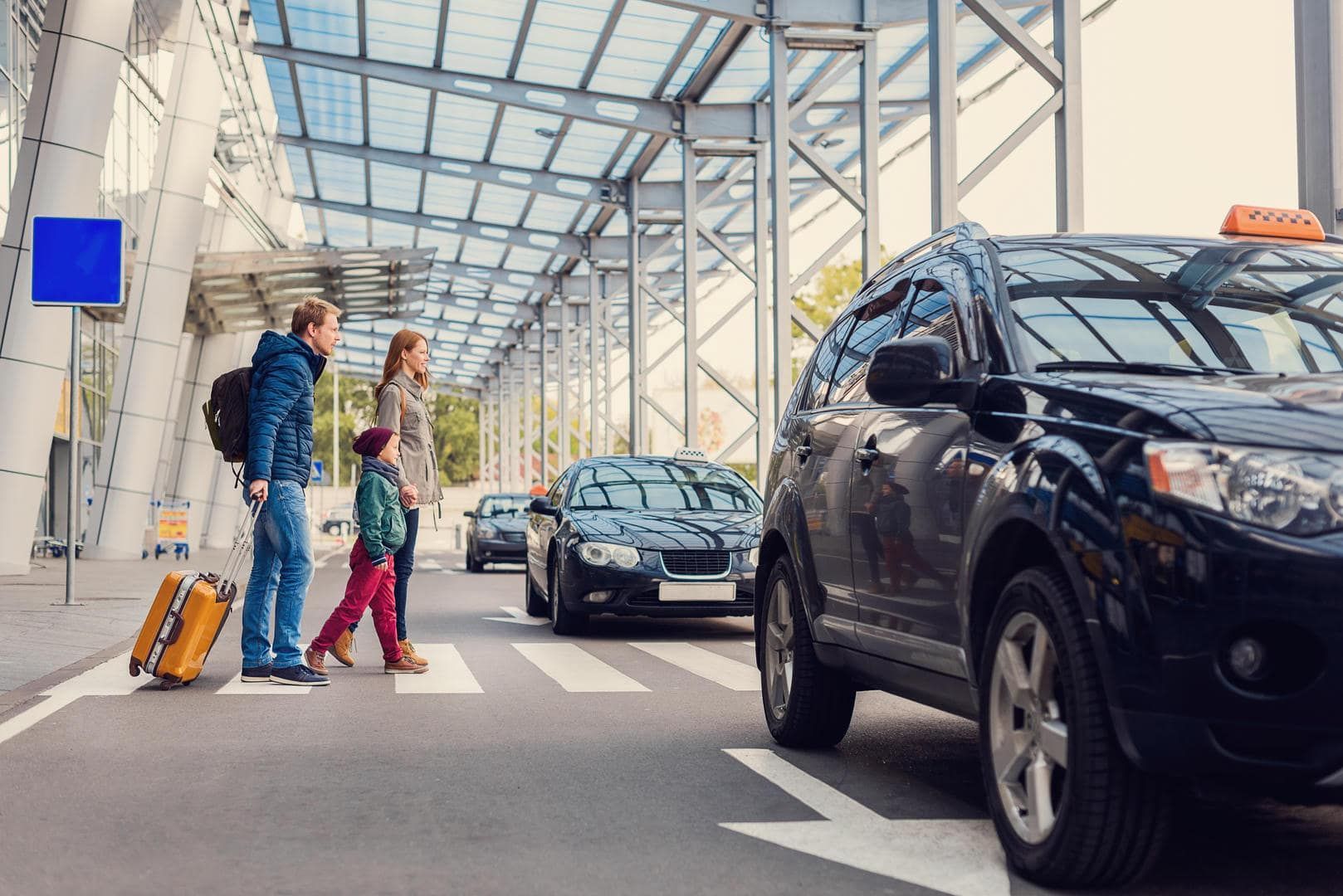A man and a woman are walking towards a taxi at an airport.